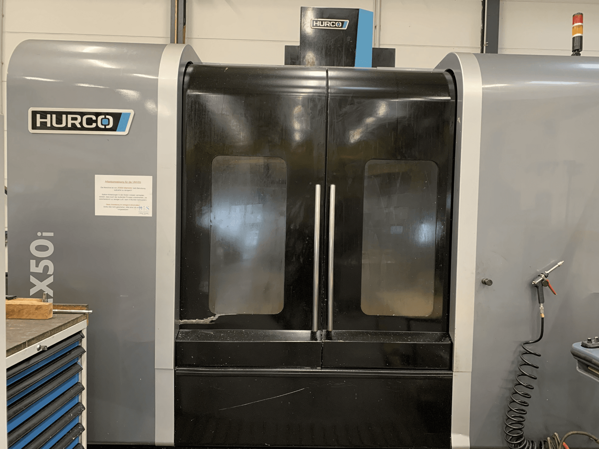 Etukuva Hurco VX50i CNC-koneesta, jossa on kaksi ovea ja jossa näkyy tekniset hallintalaitteet ja huoltokyltti sivulla.