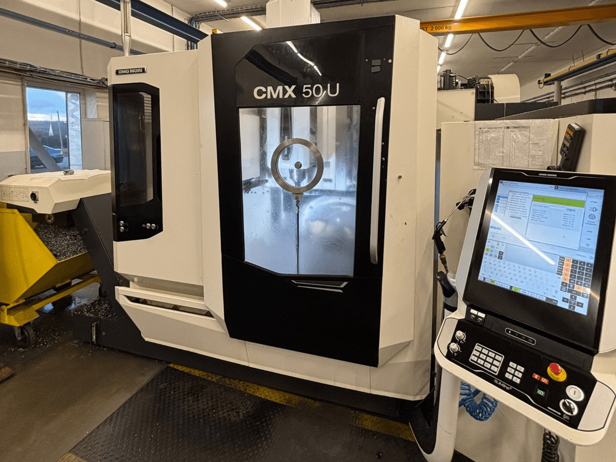 DMG MORI CMX 50 U -pystytyöstökeskus, etukuva, jossa on ohjauspaneeli ja lasinäyttö, jossa näkyy sisäinen mekaniikka.