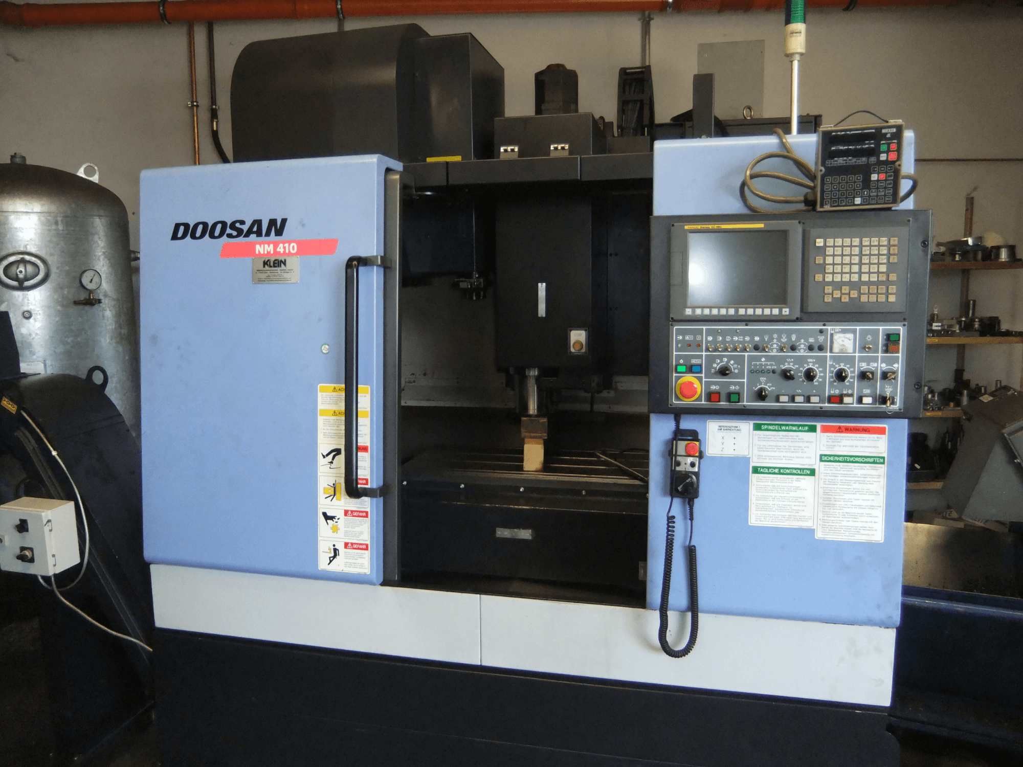 DOOSAN NM 410 -pystykoneistuskeskus, etunäkymä, jossa näkyvät ohjauspaneeli, karan alue ja turvallisuusmerkinnät.