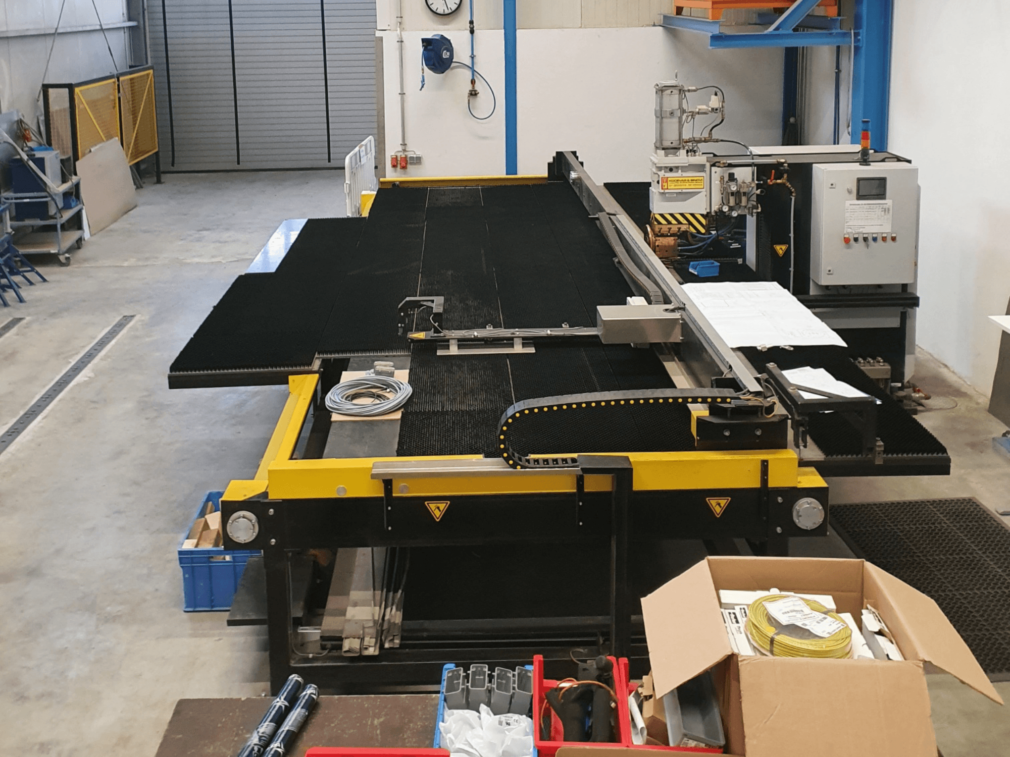 Teollisuusleikkauskone, jossa on keltaiset ja mustat piirteet, etukuva, jossa näkyy hallintalaitteet ja lisävarusteet tehdasympäristössä.