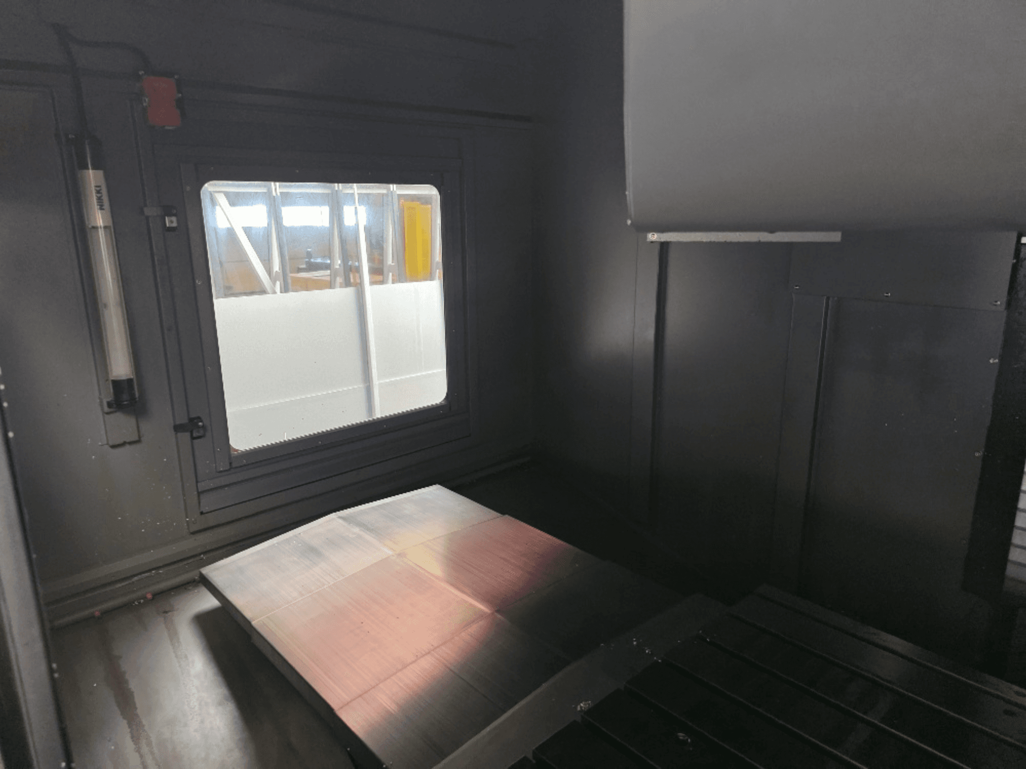 Sisäkuva konekotelosta, jossa on kiillotettu metallilevy, sivuikkuna ja minimaalinen valaistus. Merkkiä ei ole näkyvissä.