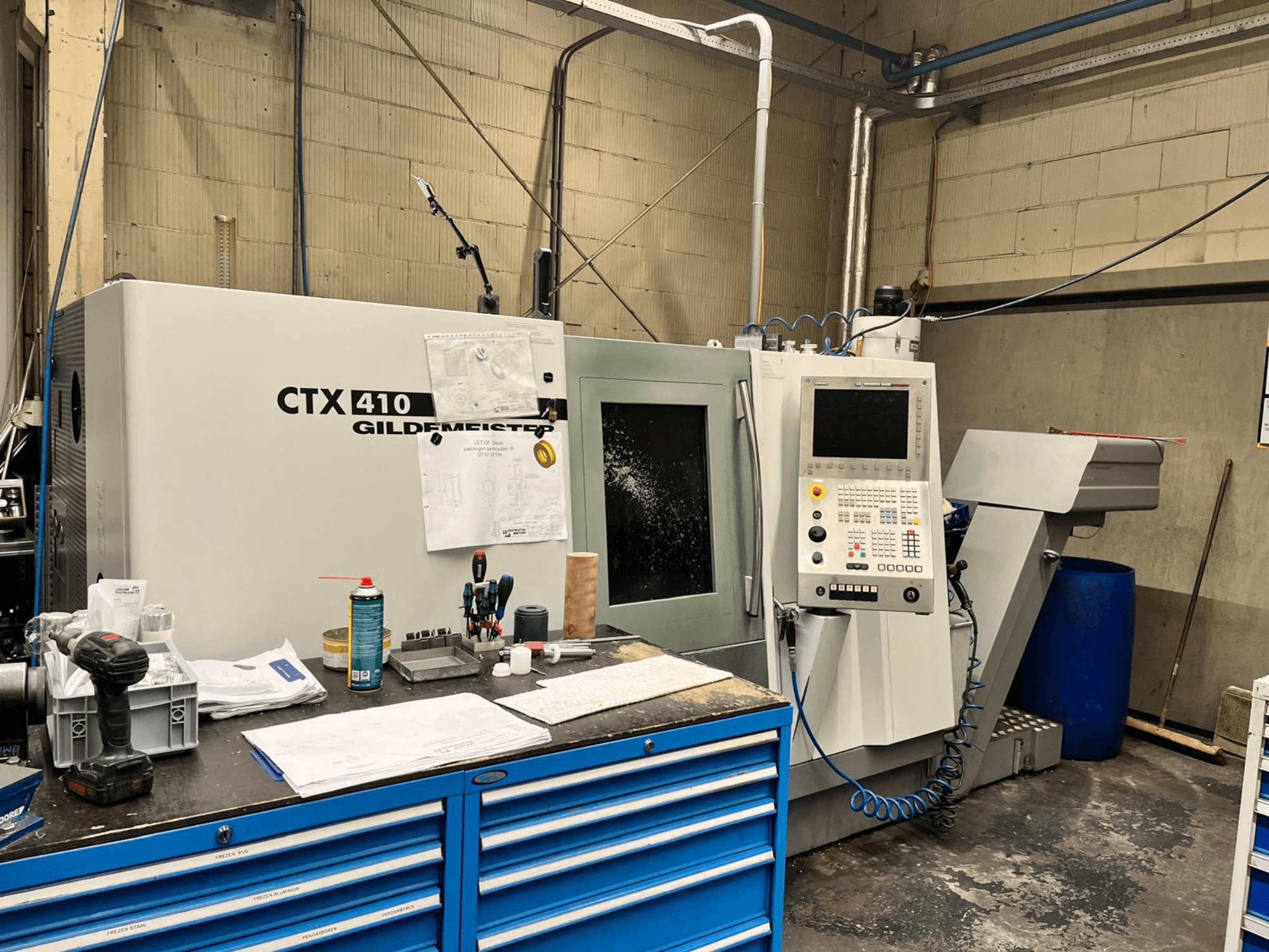 Gildemeister CTX 410 CNC-kone työpajassa, etukuva, jossa ohjauspaneeli ja erilaisia työkaluja työpöydällä.