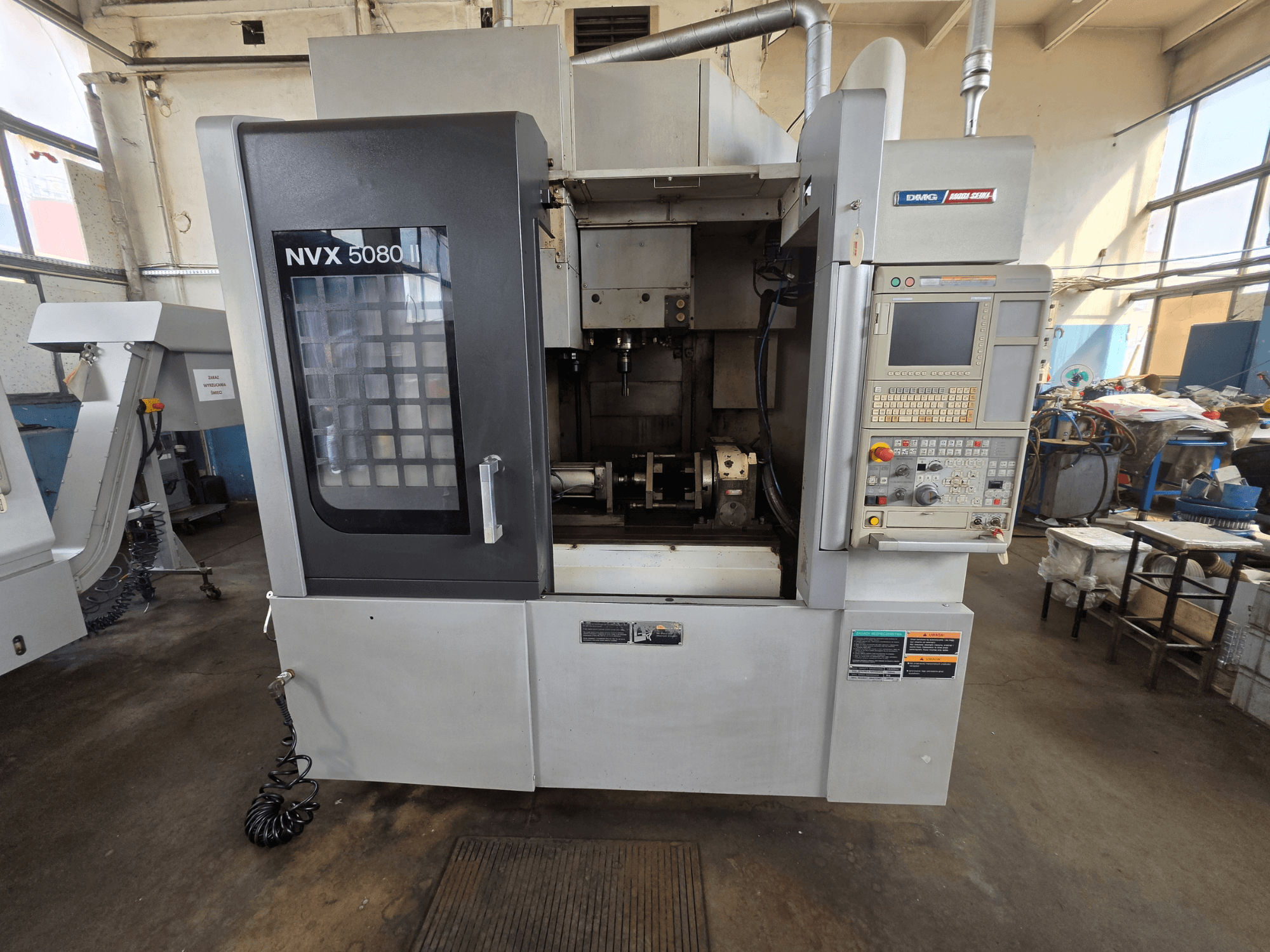 DMG Mori Seiki NVX 5080 II/40 -pystykoneistuskeskukseesta otettu etunäkymä, jossa näkyy ohjauspaneeli ja läpinäkyvä ikkuna, josta näkyy koneistusalue.