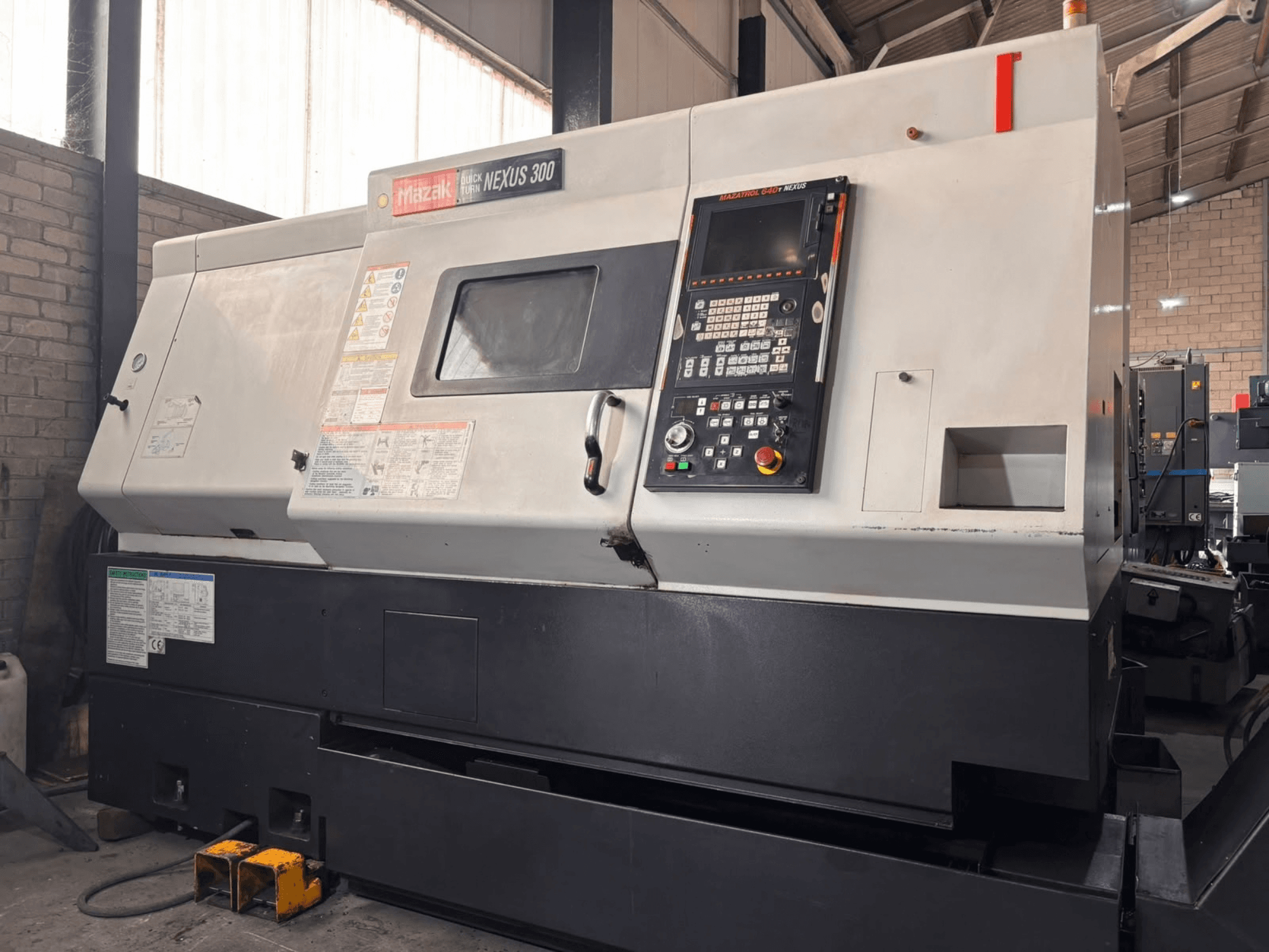 Mazak QT NEXUS 300 -vaakasuora sorvi, sivukuva, jossa näkyvät ohjauspaneeli ja toimintamerkkivalot työpajaympäristössä.