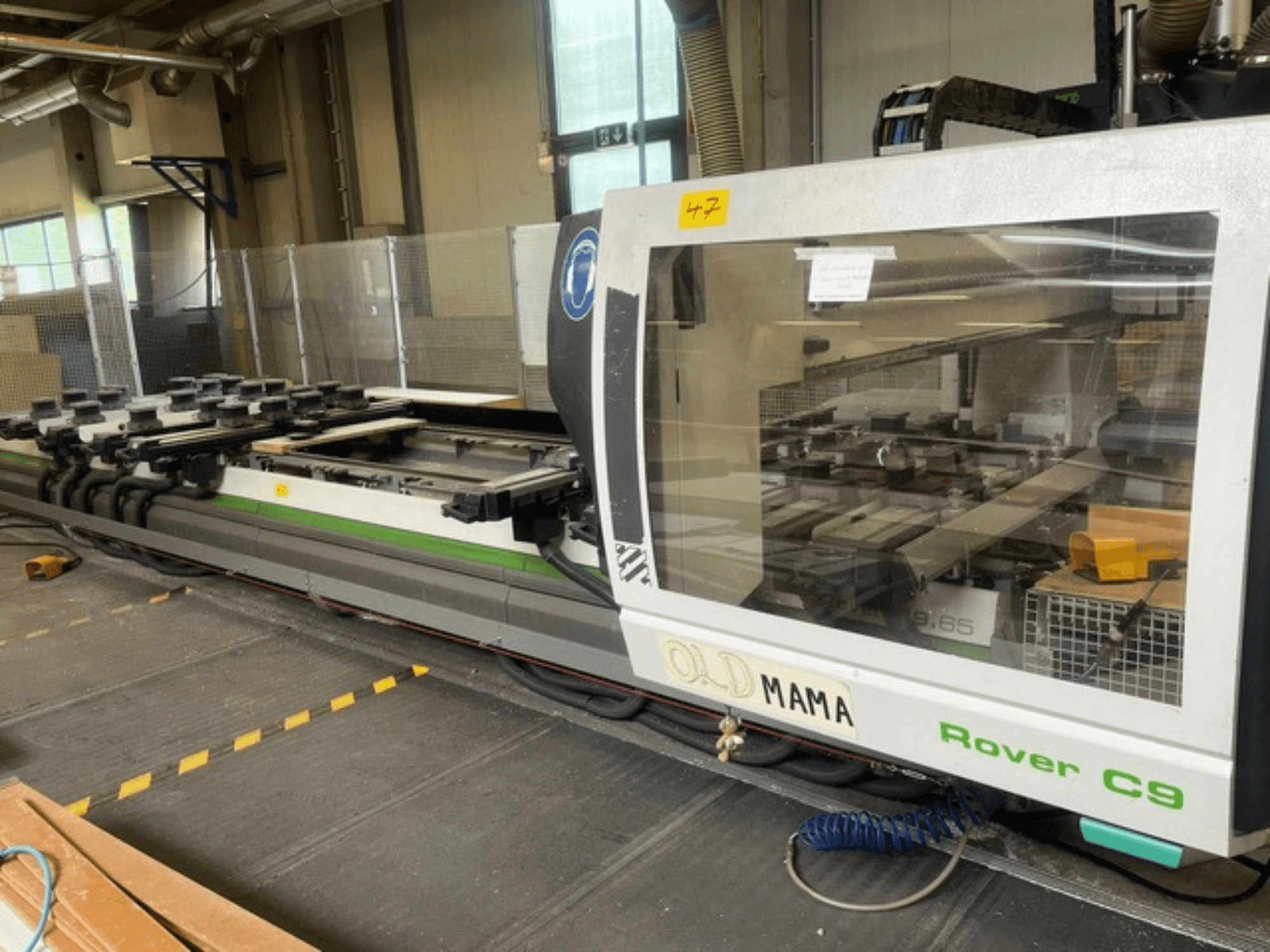 BIESSE Rover C 9.65 CNC-jyrsin työpajassa, sivukuva, jossa näkyy ohjauspaneeli ja työpöytä kiinnikkeineen.