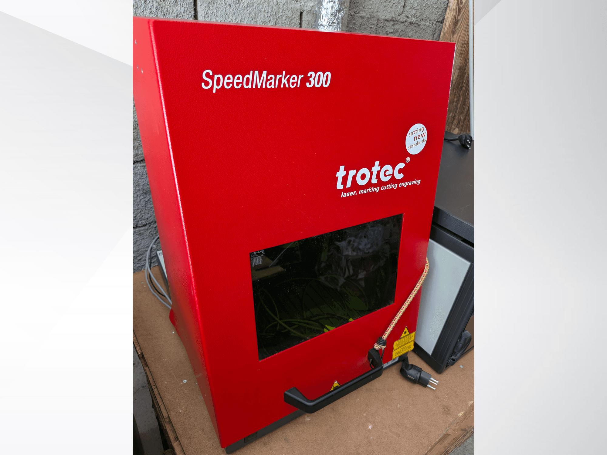 Punainen Trotec SpeedMarker 300 -lasermerkintäkone etukuvassa, jossa on suuri näyttöikkuna ja virtaliitäntä.