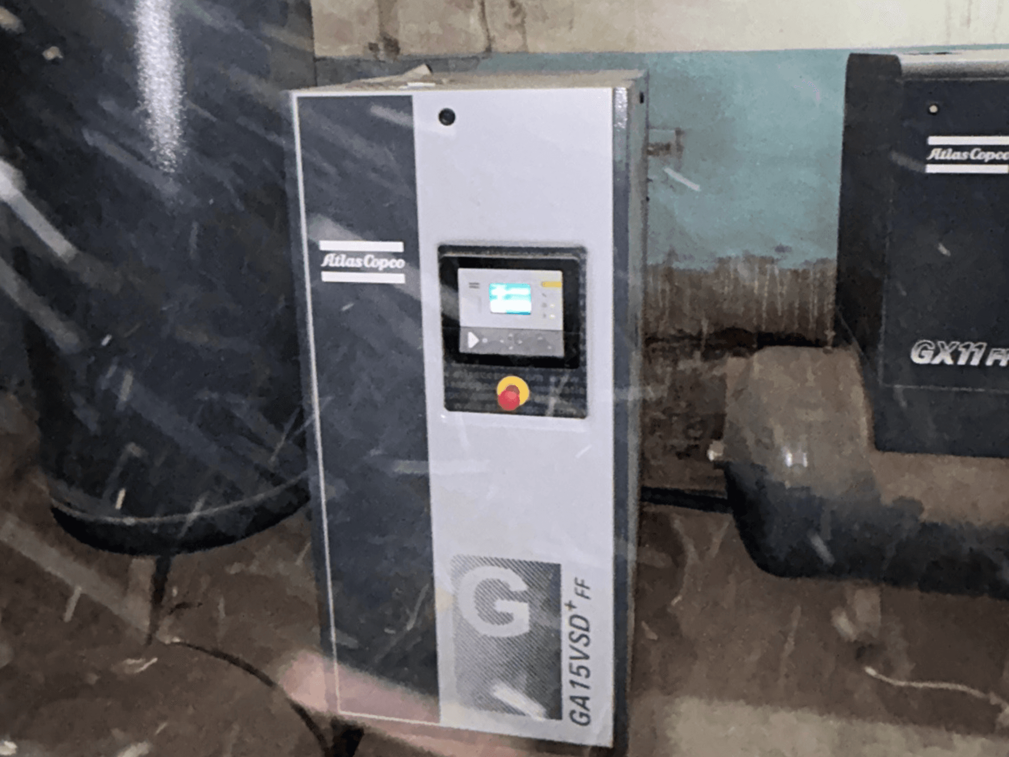 Atlas Copco GA15VSD+FF -ilmakompressori, etunäkymä; kuvassa näkyy ohjauspaneeli näytöllä ja punaisella hätäpysäytyspainikkeella.