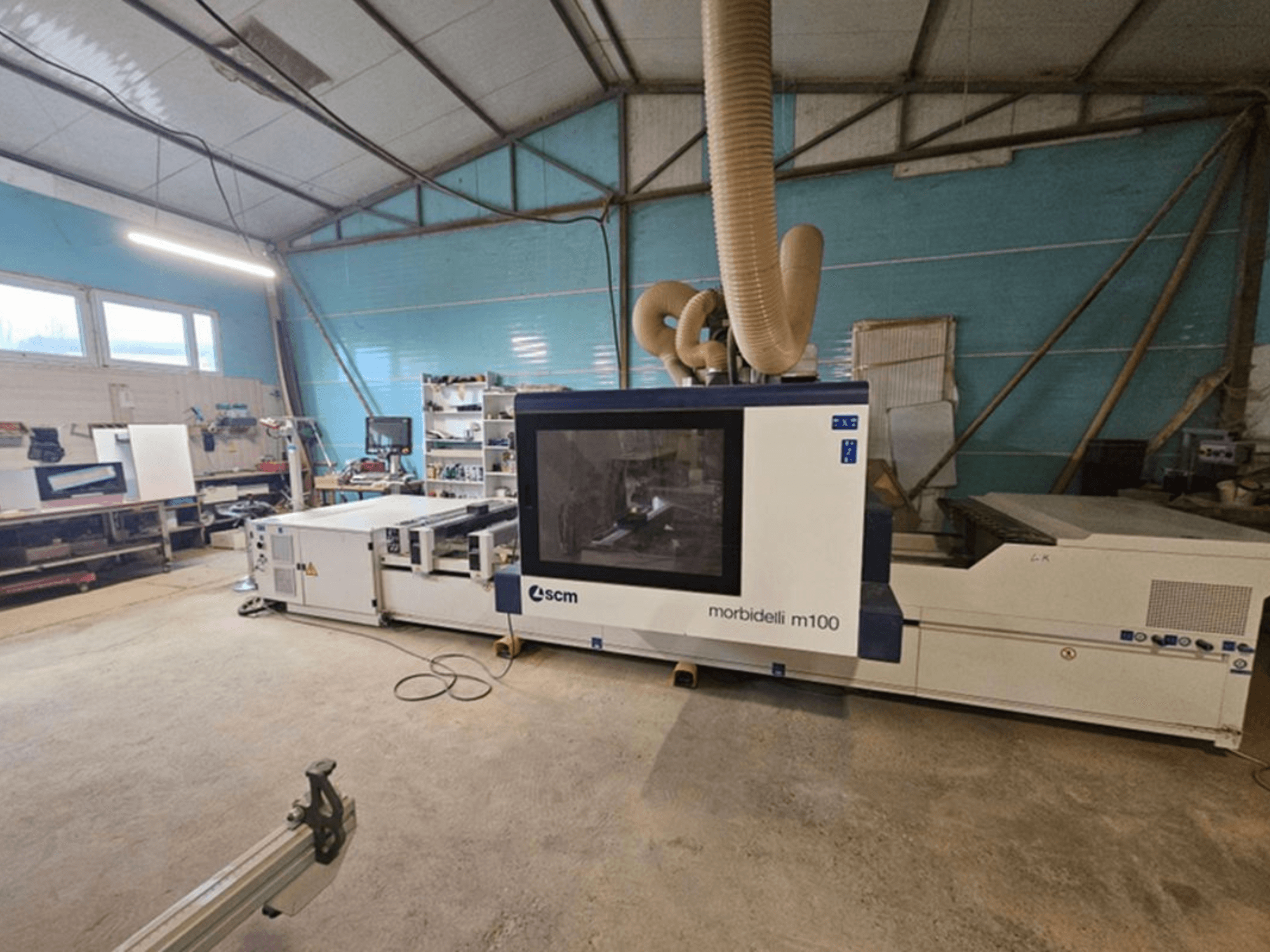 SCM MORBIDELLI M 100 CNC-työstökeskus työpajassa, etunäkymä pölynpoistojärjestelmän ja ympäröivän työtilan varusteiden kanssa.