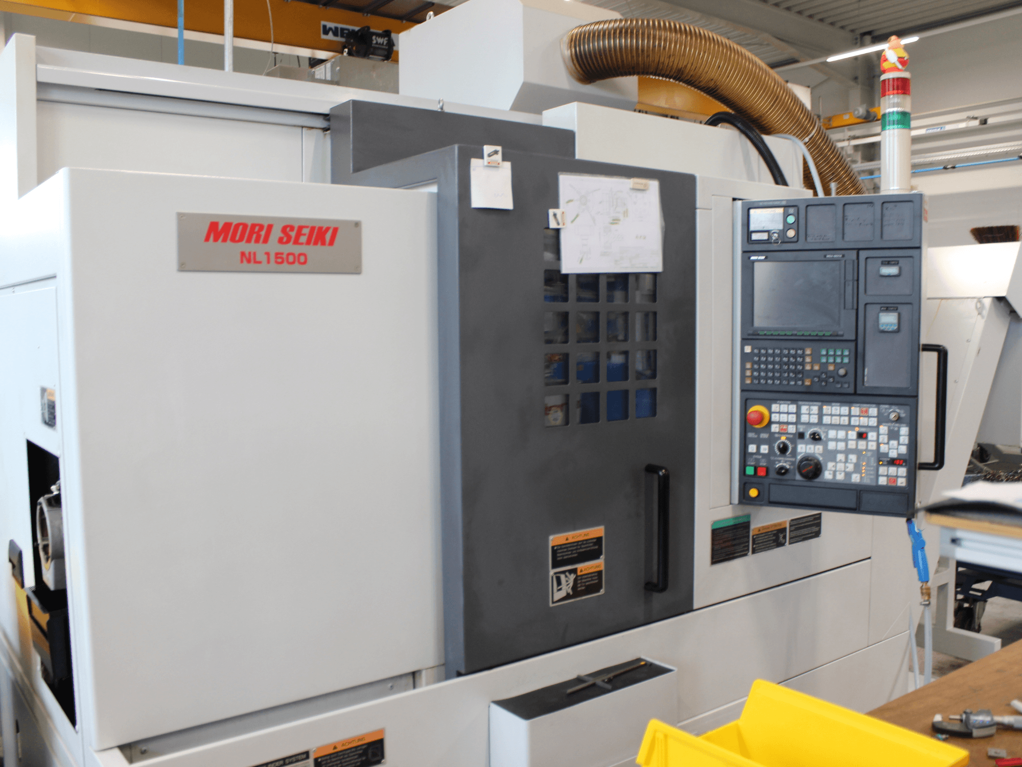MORI SEIKI NL 1500 SY -sorvaus-jyrsinkeskus sivulta katsottuna; kuvassa näkyvät ohjauspaneeli, käyttöturvallisuusmerkinnät ja jäähdytysjärjestelmä.