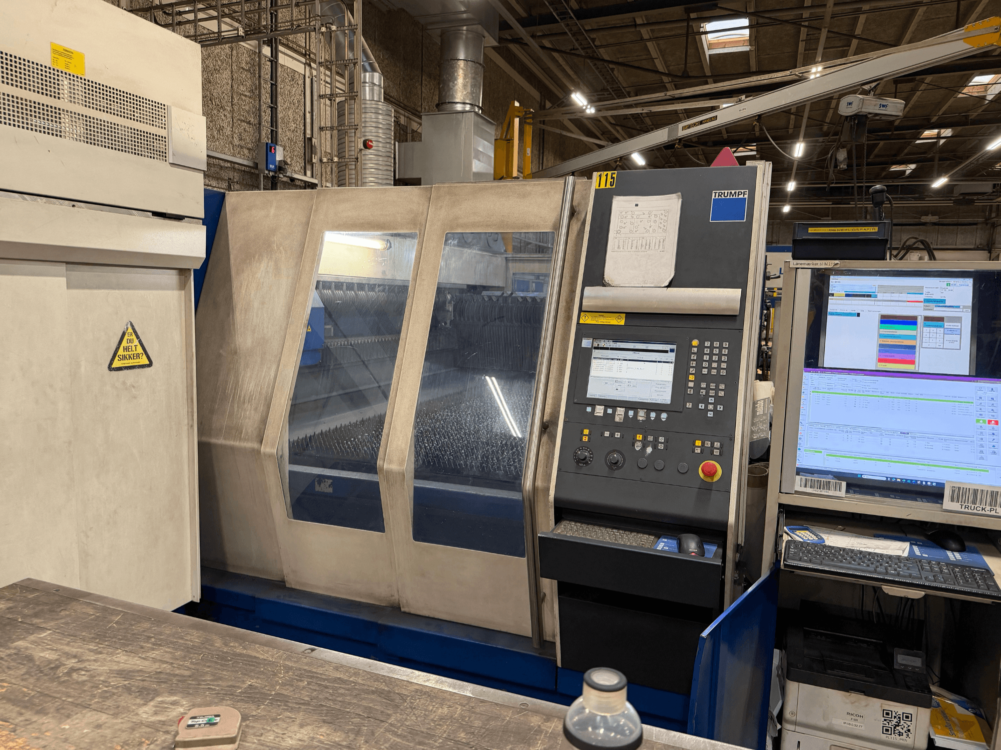 Etukuva Trumpfin teollisuuslaserkoneesta, jossa on ohjauspaneeli ja digitaalinäytöt, tehdasympäristössä.