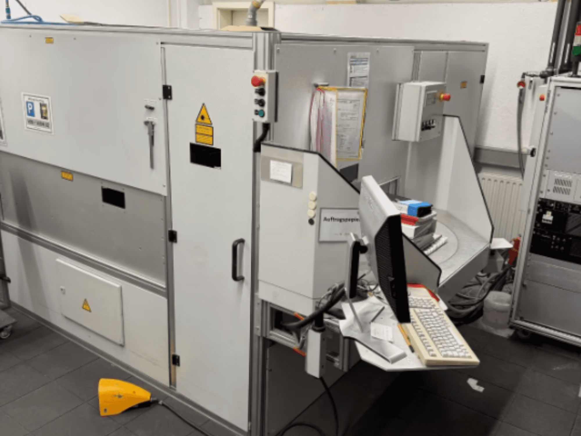 Teollisuuskone, jossa on tietokonepääte, sivukuva; sisältää ohjauspainikkeita ja turvallisuusvaroituskylttejä.