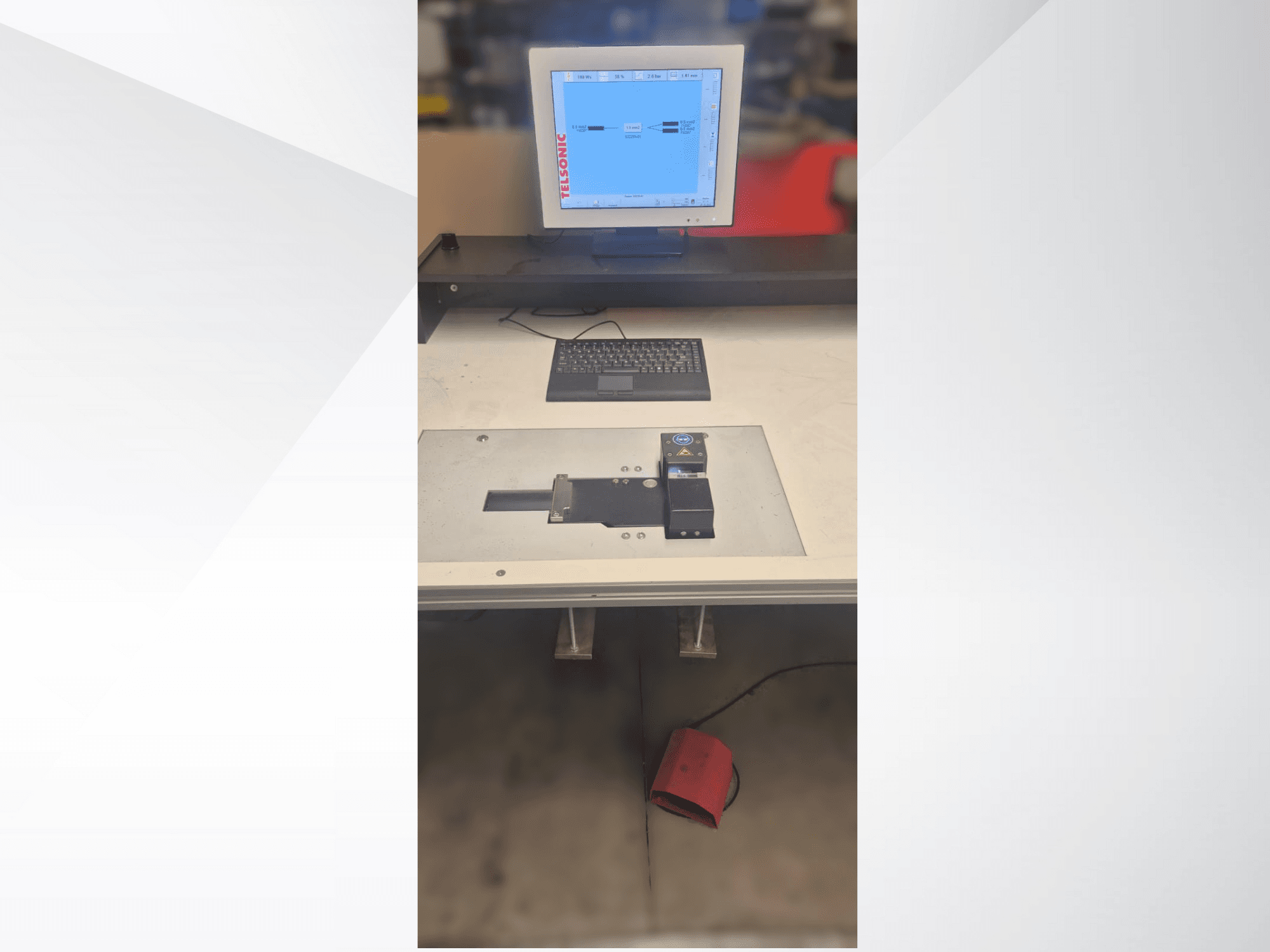Ylhäältä alas suuntautuva kuva testausasemasta, jossa on tietokonenäyttö, näppäimistö ja ohjauspaneeli, jossa on painike ja vihreä valo.