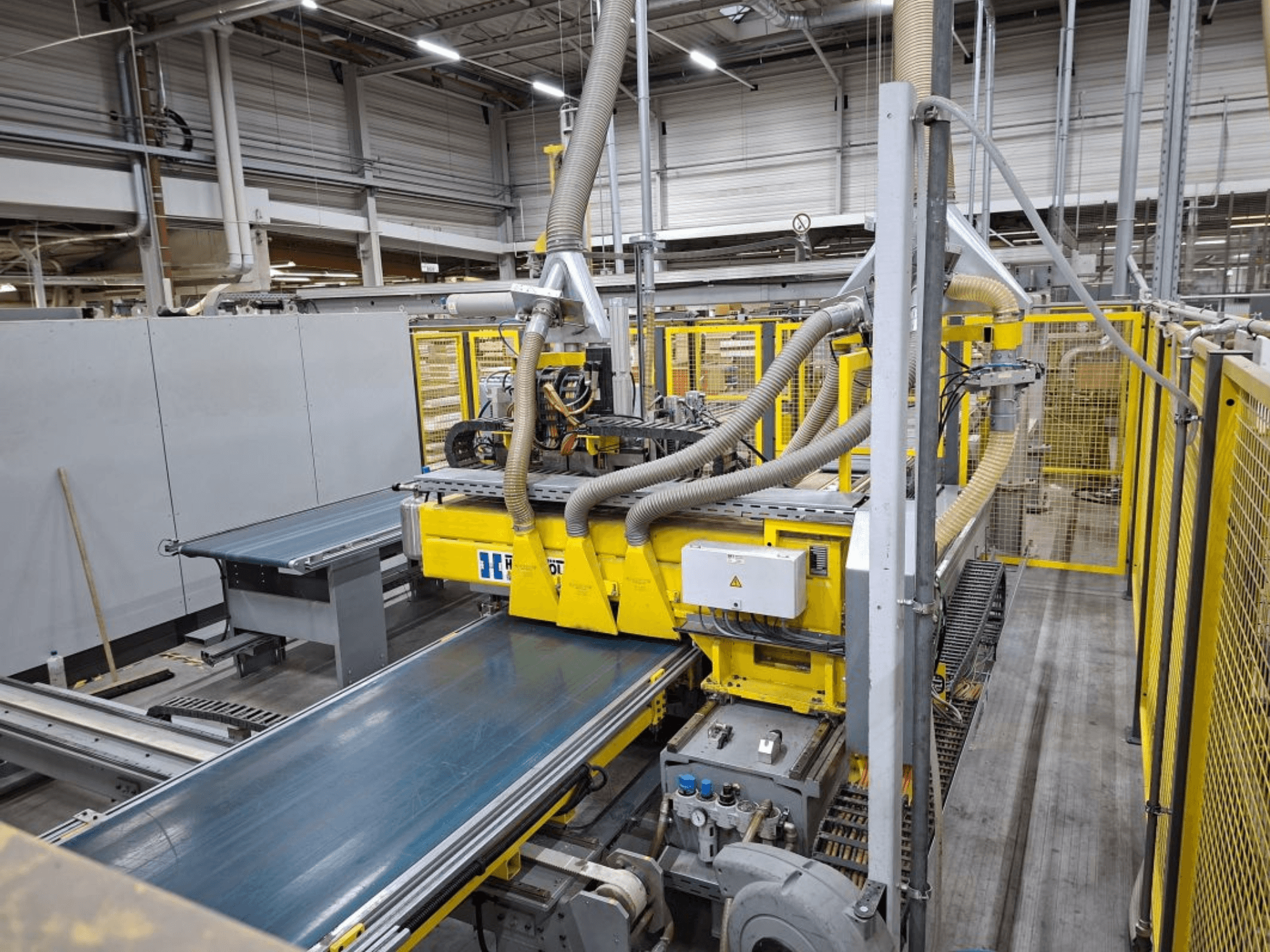 Teollisuuskuljetinjärjestelmä sivukuvasta, jossa on keltaiset koneet, ohjauspaneeli ja letkujen kiinnitysosat valmistusta varten.