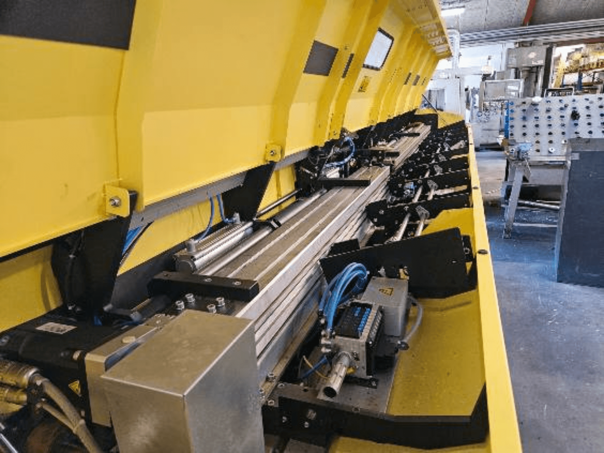 Lähikuva keltaisesta hydrauliikkakoneesta, jossa on metalliosia ja kuljetinratoja, letkuja ja elektronisia osia.