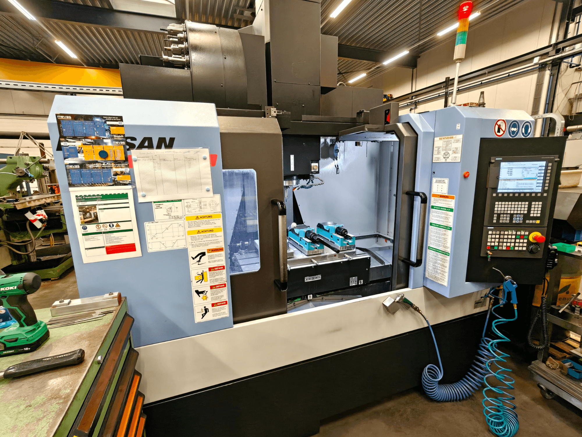 DOOSAN DNM 400 II -pystytyöstökeskus työpajassa, jossa on hallintalaitteet, työkalupidikkeet ja turvamerkinnät, etukuva.