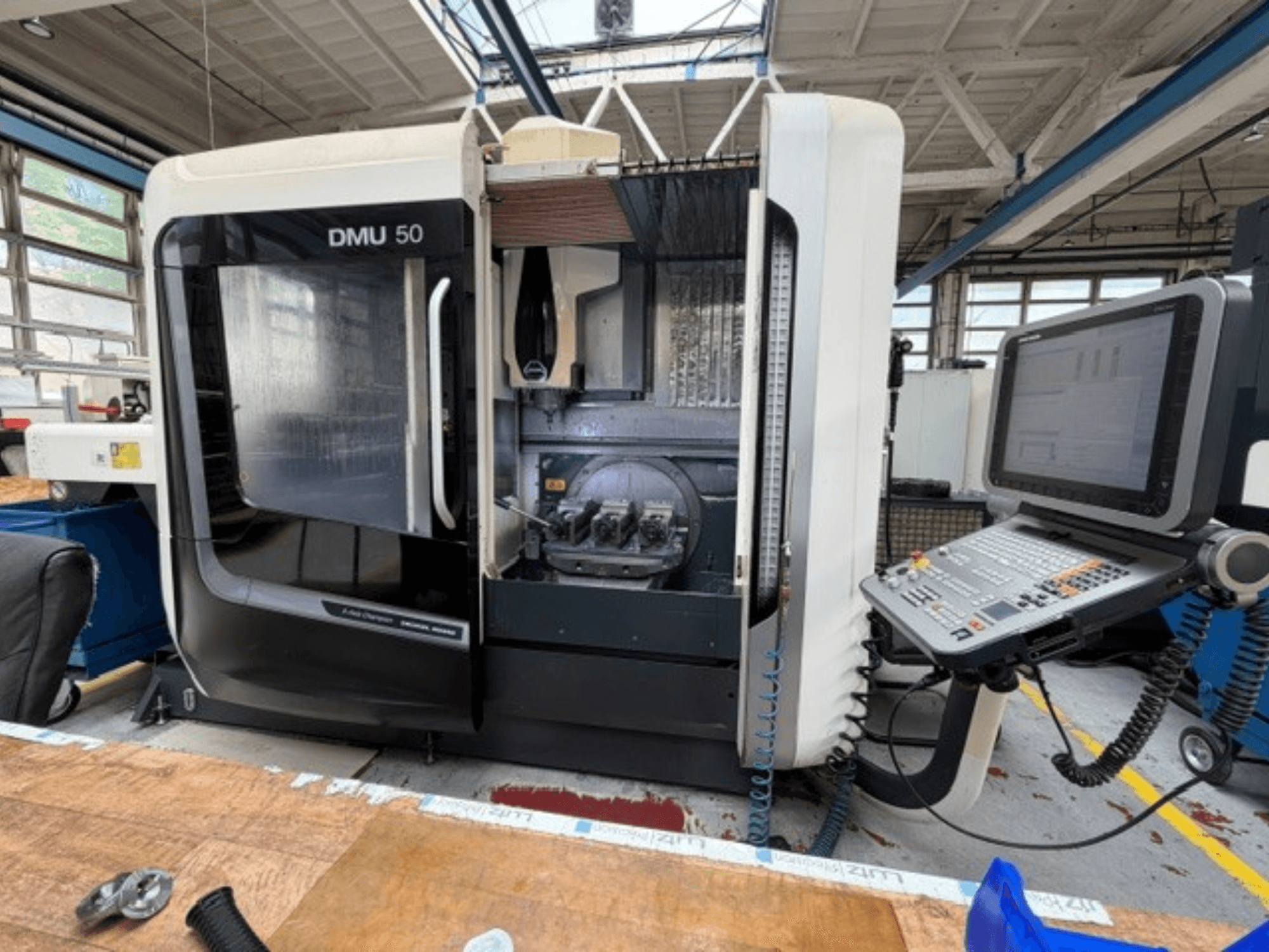 DMG MORI DMU 50 -kolmannen sukupolven pystykara-työstökeskus edestä katsottuna, ovi auki, CNC-ohjauspaneeli näkyvissä ja työstötila sisällä.