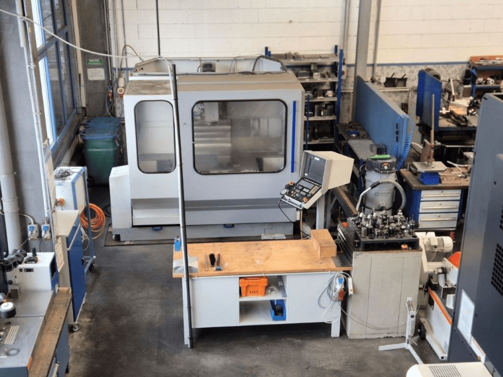 CNC-jyrsinkone työpajassa, etukuva, taustalla ohjauspaneeli, työtaso ja työkalut.