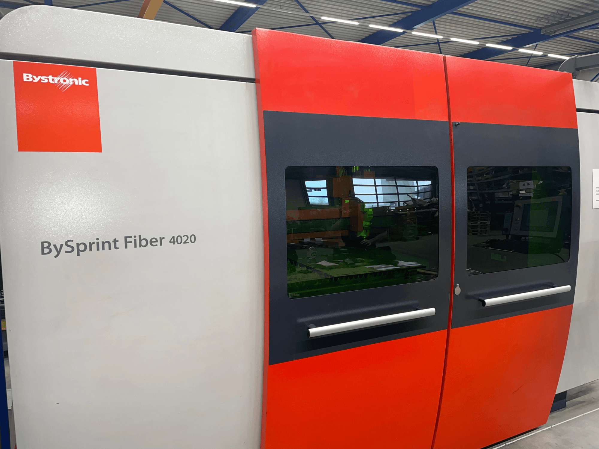 Bystronic BySprint Fiber 4020 edestä katsottuna, harmaa ja punainen paneelirakenne, jossa on suuret ikkunat ja sisäpuolella näkyvä käyttöliittymä.