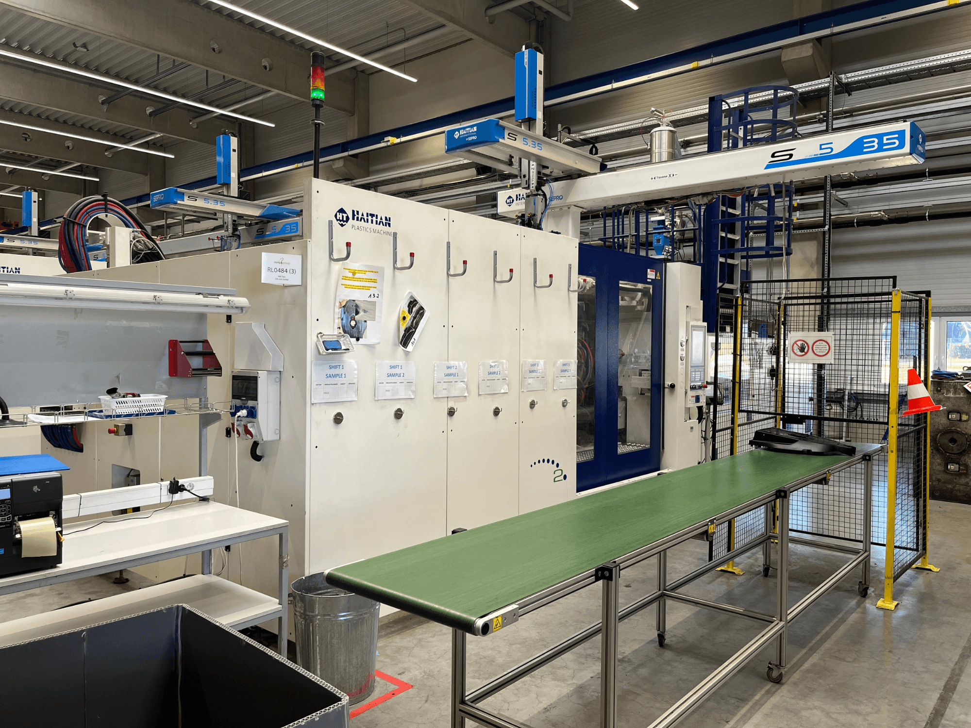 Haitilainen S5-35-muovikone työpajassa; vihreä kuljetuspöytä, suojakaiteet ja ohjauspaneeli näkyvät edestä.