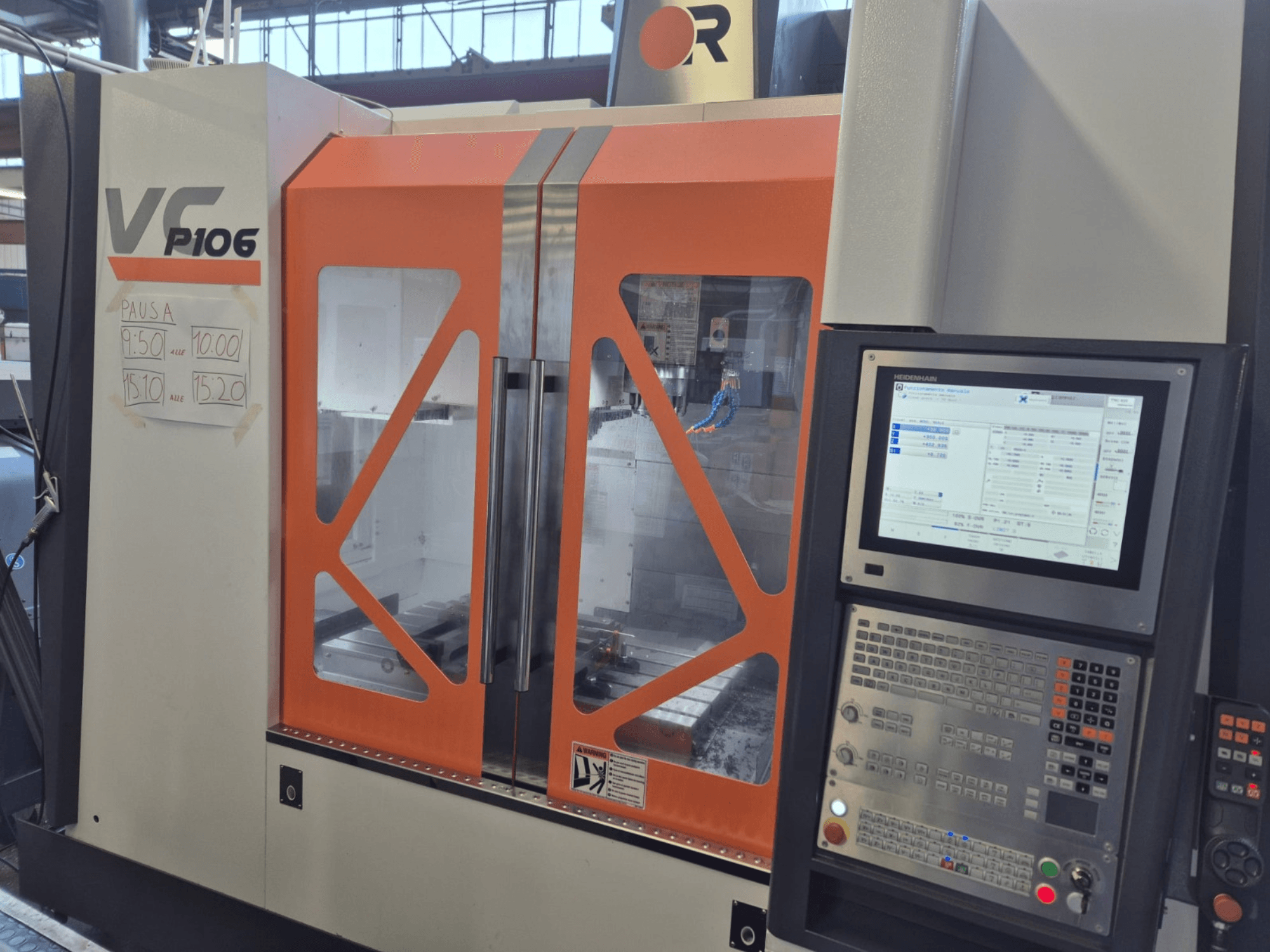 Alt-teksti: VF P106 CNC-kone, etukuva, jossa näkyy ohjauspaneeli ja paperille kirjoitetut suunnitellut toiminta-ajat: Oranssi ja harmaa VF P106 CNC-kone, etukuva.