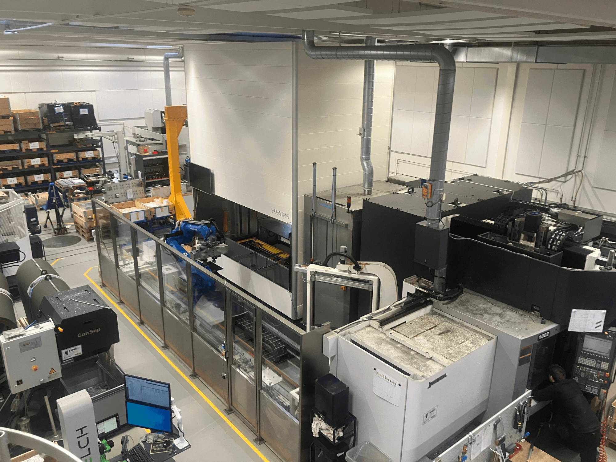 SSI SCHAFER Logimat -automaatiojärjestelmä varastossa, etukuva; robottivarsi, varastohyllyt ja koneet.