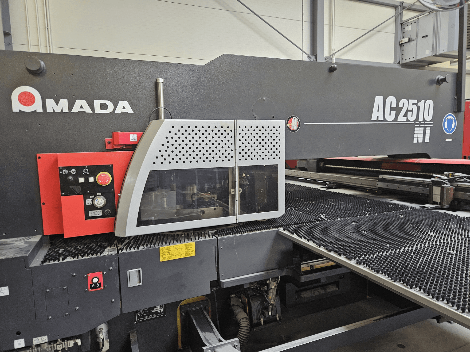 Amada AC2510 NT -laserleikkauskone, etukuva, jossa on ohjauspaneeli, jossa on nupit, painikkeet ja suojakansi.