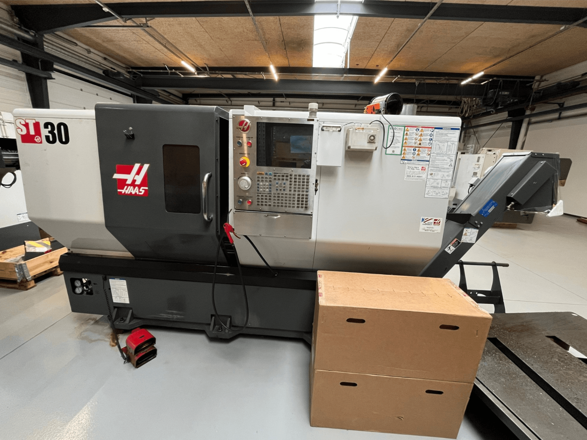 Haas ST-30 CNC-sorvi, etukuva, jossa on ohjauspaneeli painikkeilla, hätäpysäytys ja kaksi pinottua pahvilaatikkoa.
