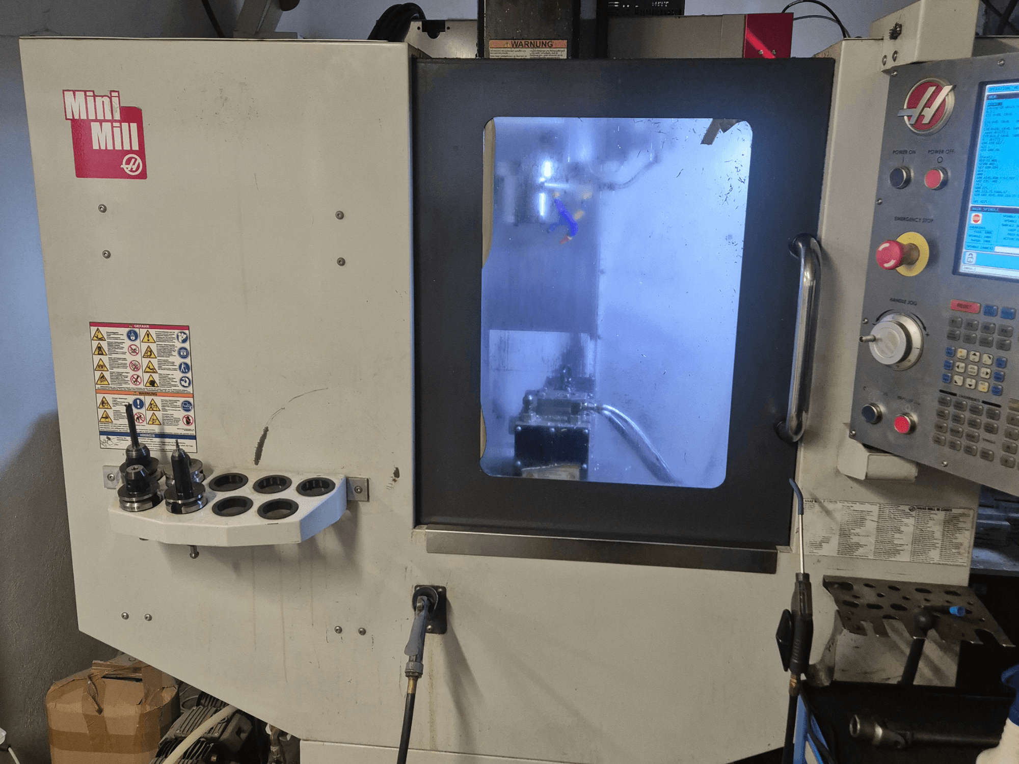 HAAS Mini Mill -jyrsimen etukuva, jossa näkyy ohjauspaneeli, työkalunpitimet ja näkymä työstöalueelle jäähdytysnesteen kanssa.