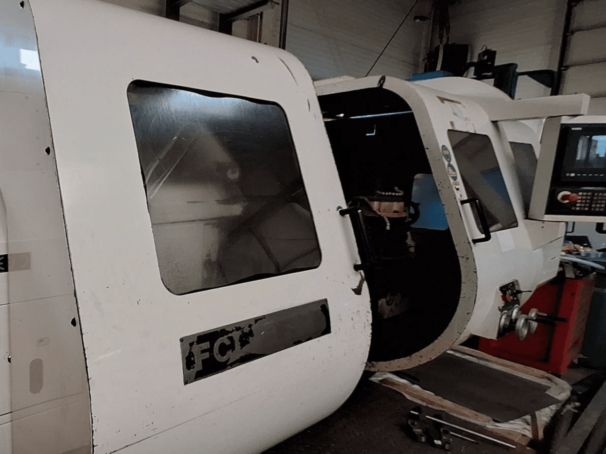 Valkoinen CNC-kone, jossa on näkyvä ohjauspaneeli ja avoin ovi, jossa näkyy sisätilojen komponentit; etukuva. Tuotemerkki: FCT.