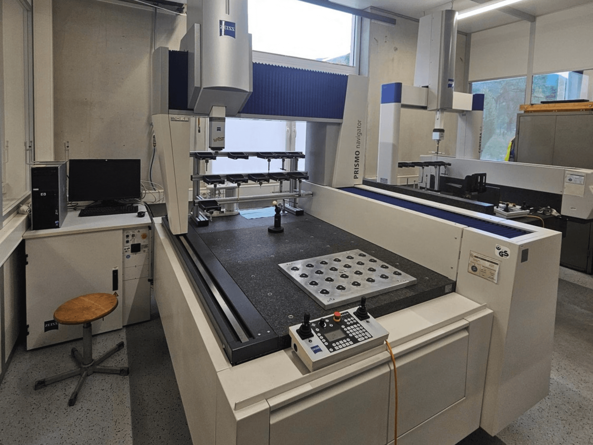 ZEISS Prismo Navigator 7 -koordinaattimittauskone laboratoriossa; etunäkymä, jossa näkyvät ohjauspaneeli, työpöytä ja näyttö.