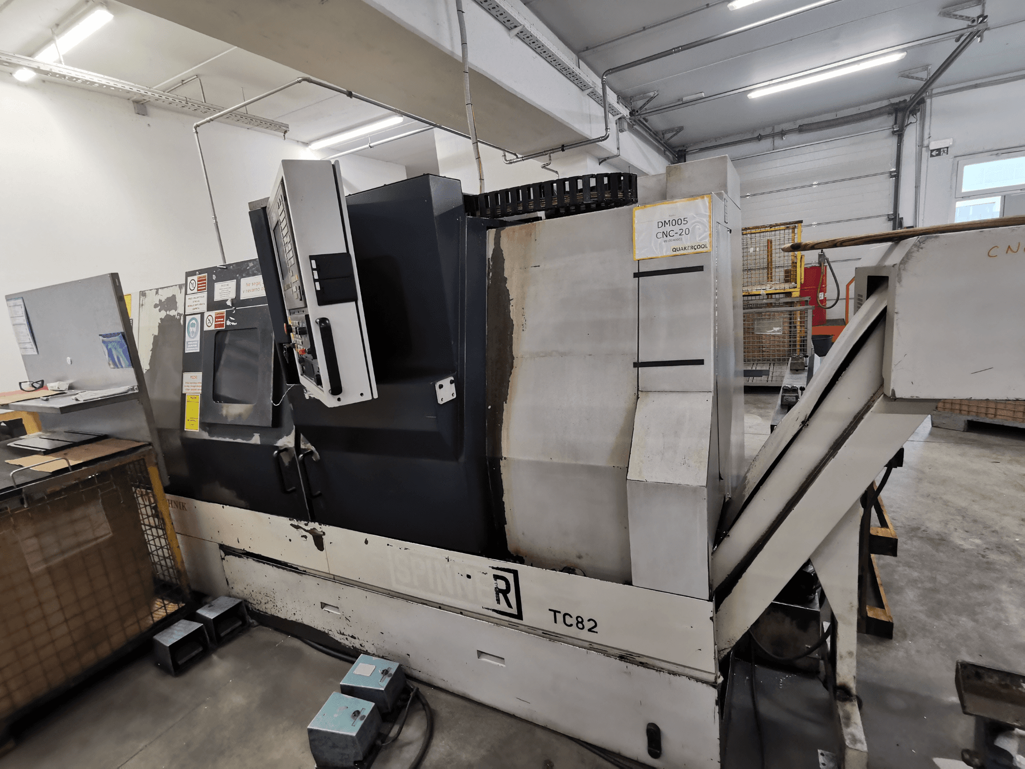 CNC-kone, tuotemerkki Spinner, malli TC82, sivukuva, jossa näkyy ohjauspaneeli ja romunpoistokouru korjaamolla.