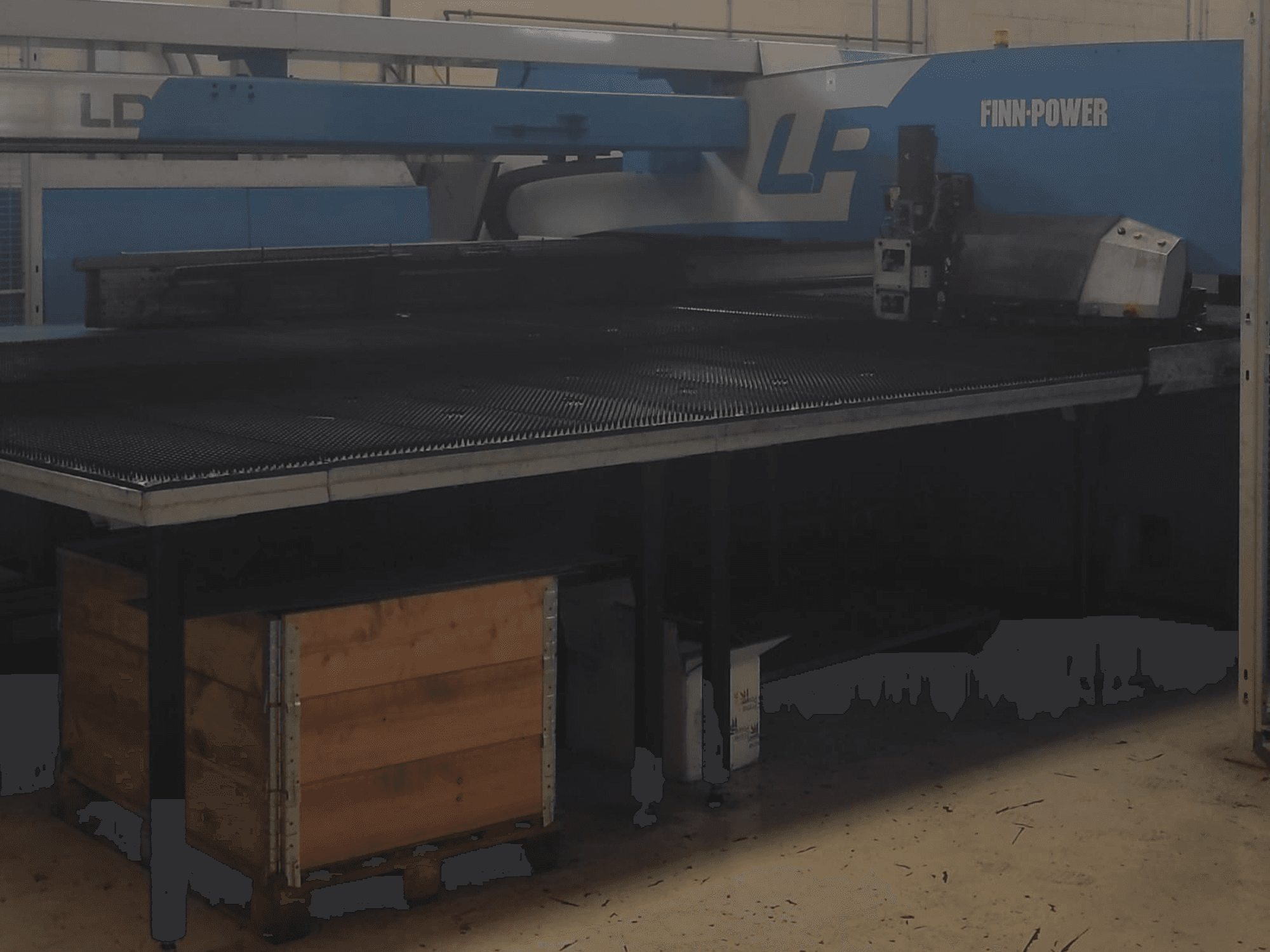 Finn-Power LP-leikkuukone tehtaalla, etukuva, jonka alla on kuvioitu metallipöytä ja puulaatikko.