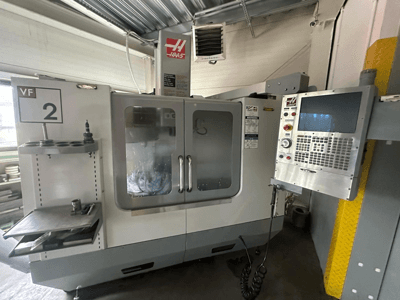 Haas VF-2 CNC-kone, etukuva, jossa on hallintalaitteet, työkalunpidin ja läpinäkyvät ovet, joissa työkalut ovat näkyvissä kaapin sisällä.