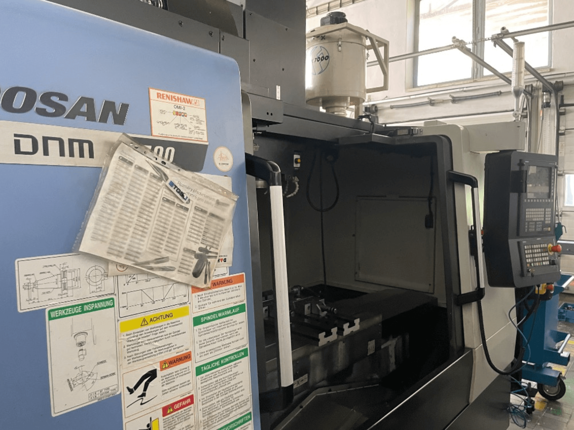 DOOSAN DNM 5700 -pystytyöstökeskus, etukuva, jossa näkyy ohjauspaneeli, turvatarrat ja koneen tiedot.