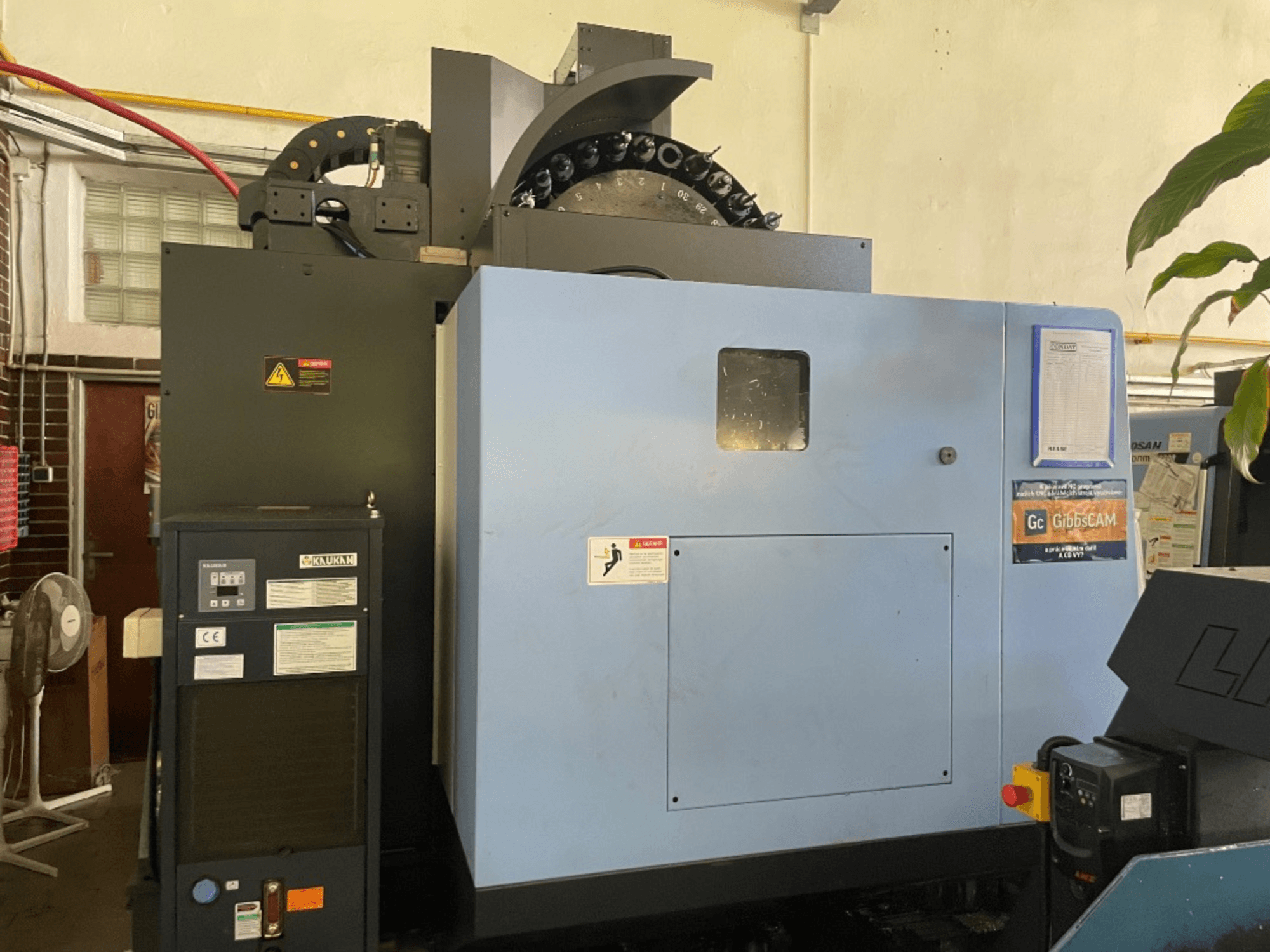 DOOSAN DNM 5700 -pystytyöstökeskuksen etukuva, jossa näkyy ohjauspaneeli, turvatarrat ja koneen ominaisuudet.