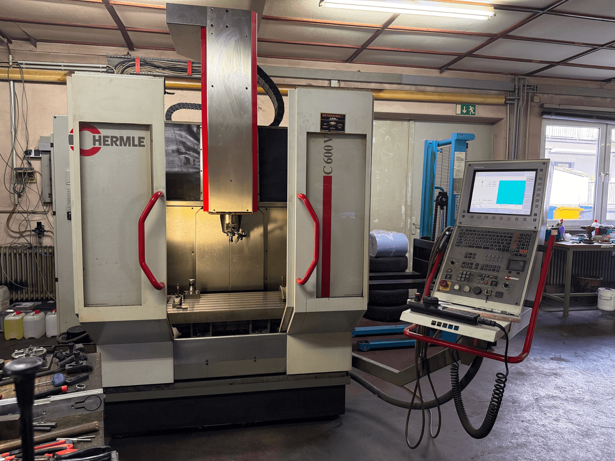 Hermle C 600 CNC-jyrsinkone etukuvasta, jossa on ohjauspaneeli, jossa on lukuisia painikkeita, ja tilava työskentelyalue.