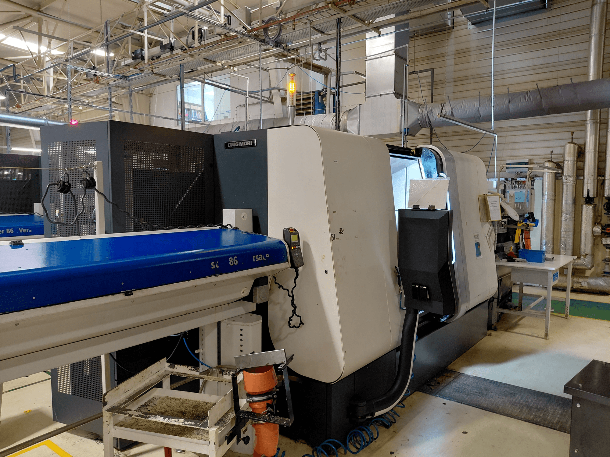 DMG MORI Sprint 65 lineaarinen monikarainen sorvauskone, sivukuva, jossa ohjauspaneeli ja kuljetin näkyvät työpajassa.