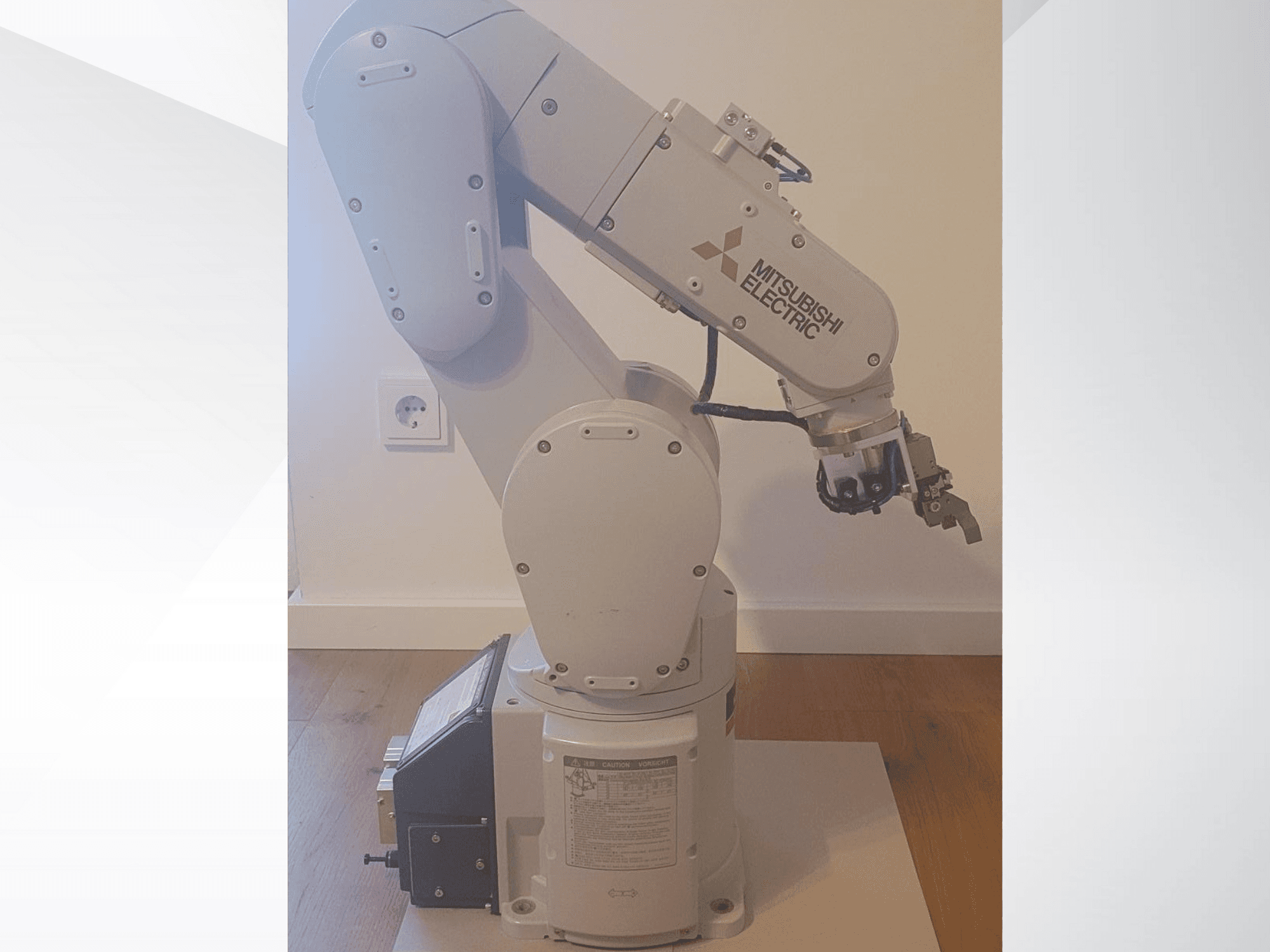 Mitsubishi Electricin robottikäsivarsi, sivukuva, jossa on tarttuja ja yksityiskohtainen ohjauspaneeli pohjassa käyttöasetuksia varten.