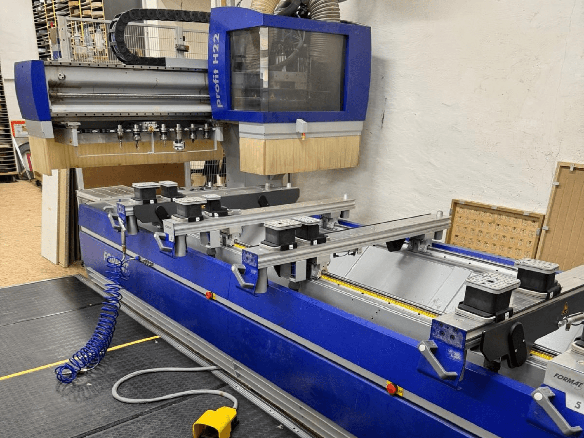 FORMAT4 PROFIT H22 CNC-puunkäsittelykeskus, etunäkymä, jossa sinisellä rungolla näkyvät työstötyökalut ja kiinnityspidikkeet.