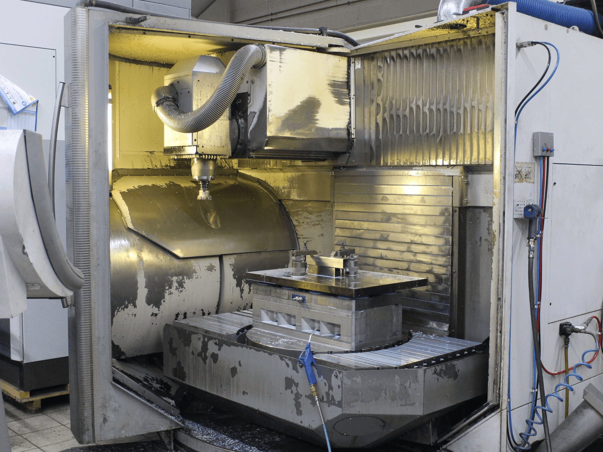 CNC-jyrsinkoneen sisätila, sivukuva, jossa näkyy työkappale ja leikkuutyökalu, jossa on metallilastuja ja jäähdytysnestejäämiä.