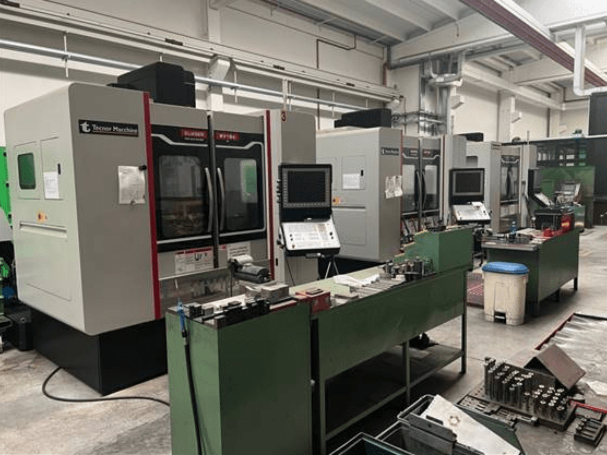 Neljä Tecnoer Marchinen CNC-konetta työpajassa, etukuva, työkalut ja osat vihreillä työpöydillä.