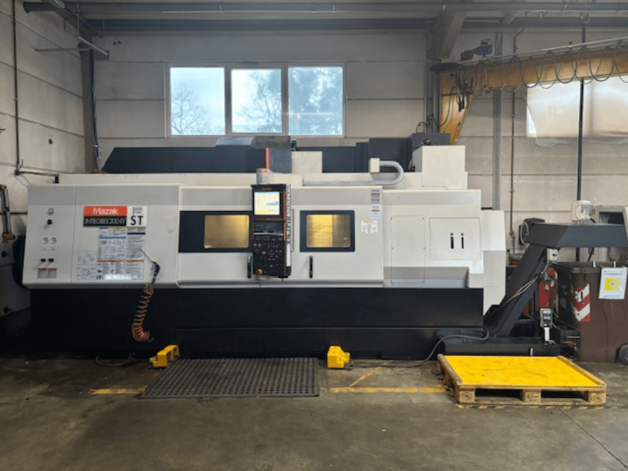Mazak Integrex 200 SY ST, sivukuva, jossa näkyy ohjauspaneeli, toimintanäytöt ja jäähdytysnesteen johdot korjaamolla.
