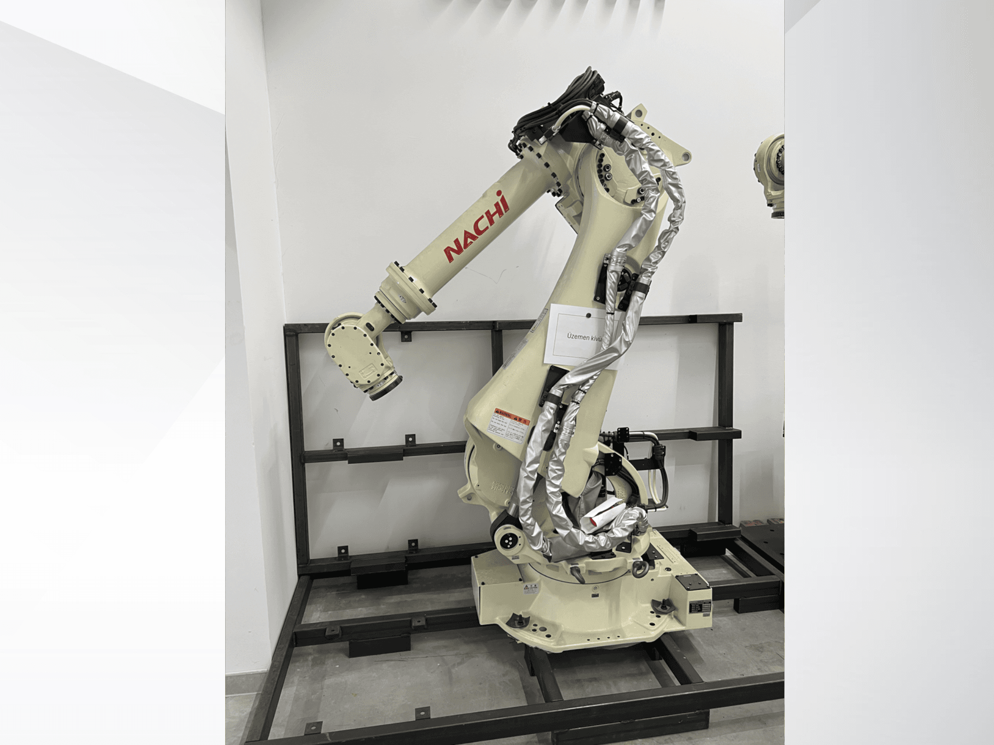 NACHI SRA166-01 -robottivarsi sivukuvassa, jossa on joustavat nivelet, kiinnitetyt kaapelit ja joka on asennettu suojakehykseen.