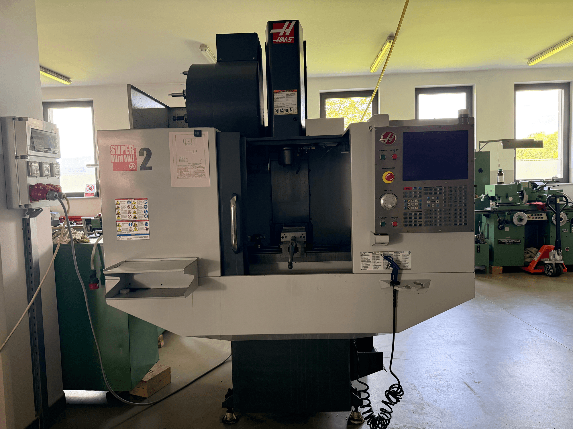 Haas Mini Mill 2 -pystytyöstökeskus etukuvassa, jossa näkyy ohjauspaneeli ja työkalualue varoituskyltteineen.