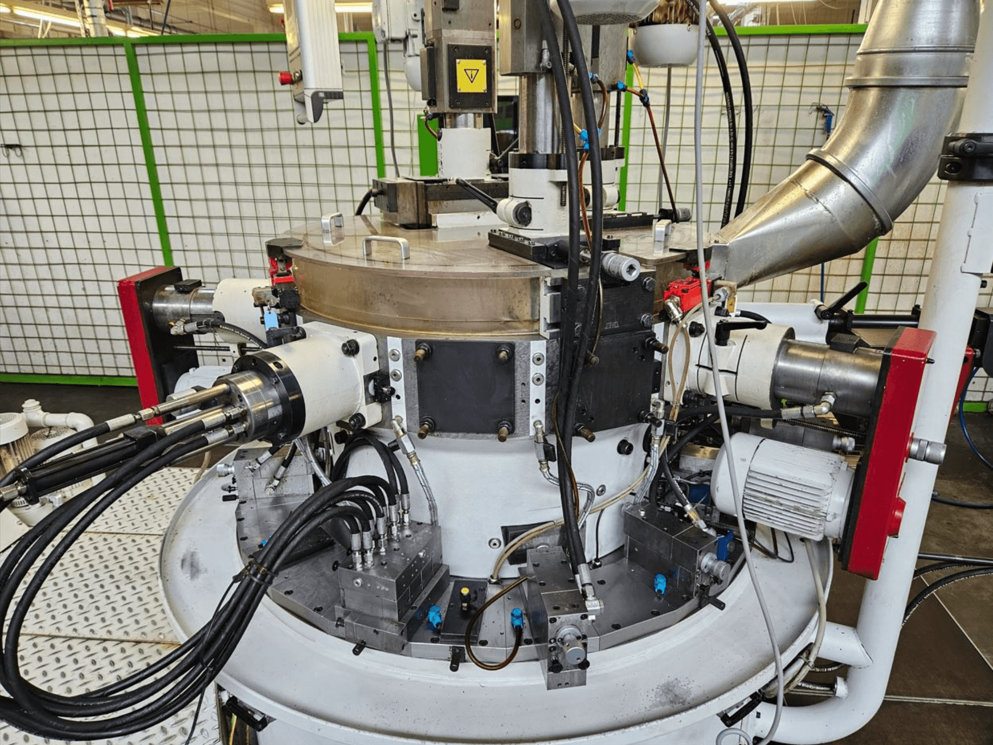 Lähikuva teollisuuskoneesta, jossa on hydrauliletkuja, metalliosia ja pyörivä alusta. Merkkiä ei näy.