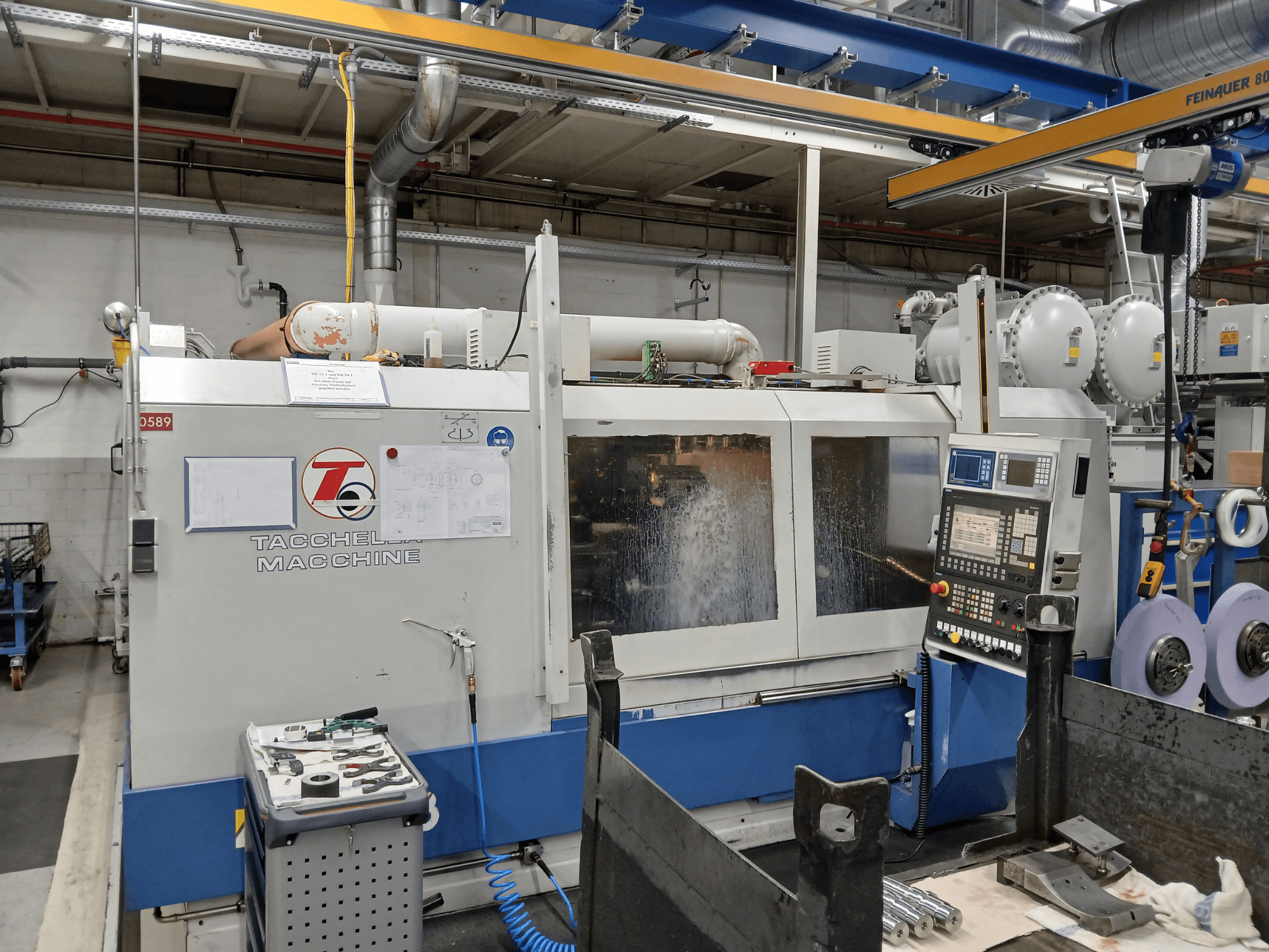 Tacchella-työstökeskus edestäpäin, ohjauspaneeli ja työkalut näkyvissä. Jäähdytysneste suihkuaa käytön aikana.