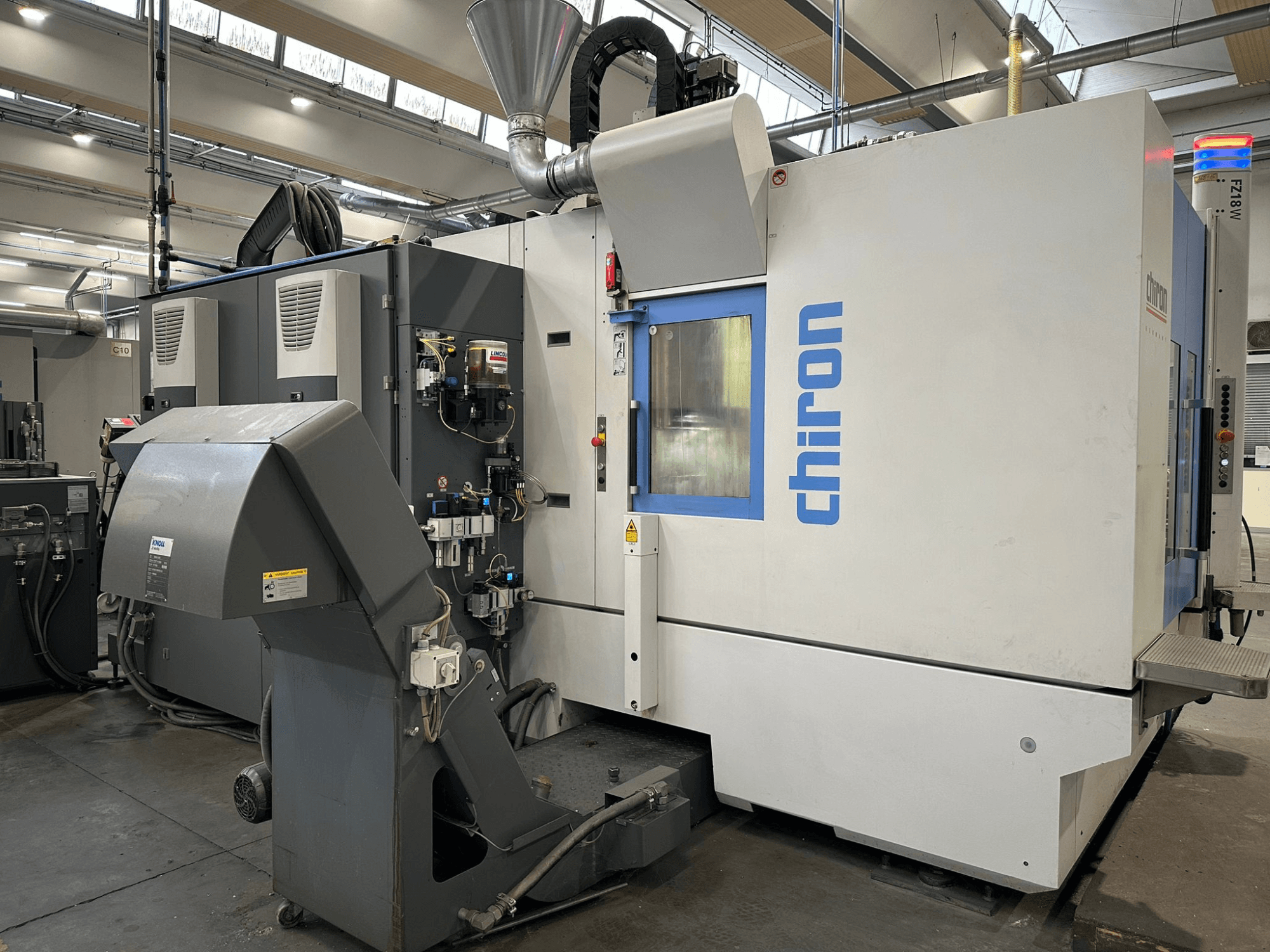 Harmaavalkoinen Chiron CNC-kone, etukuva, jossa on hallintalaitteet, putket ja pölynpoistohuppu.