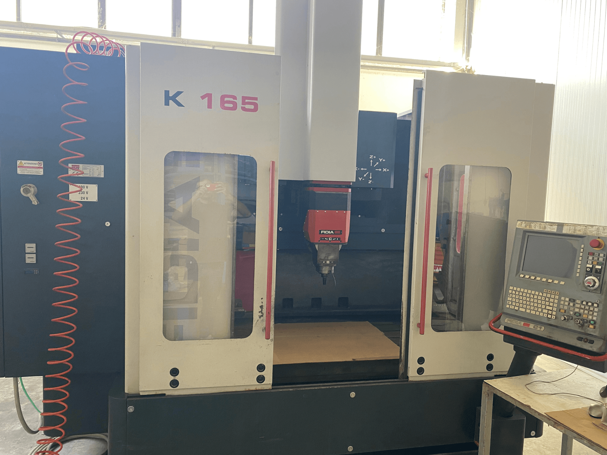 Fidia K 165 CNC-kone, jossa on punainen kara ja ohjauspaneeli, edestä katsottuna hyvin valaistussa työpajassa.