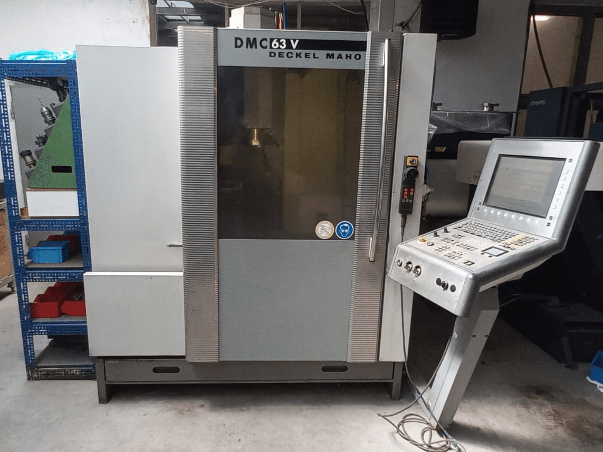DMG DECKEL MAHO DMC 63V -pystykoneistuskeskukseen etunäkymä, jossa näkyvät ohjauspaneeli ja työtila.