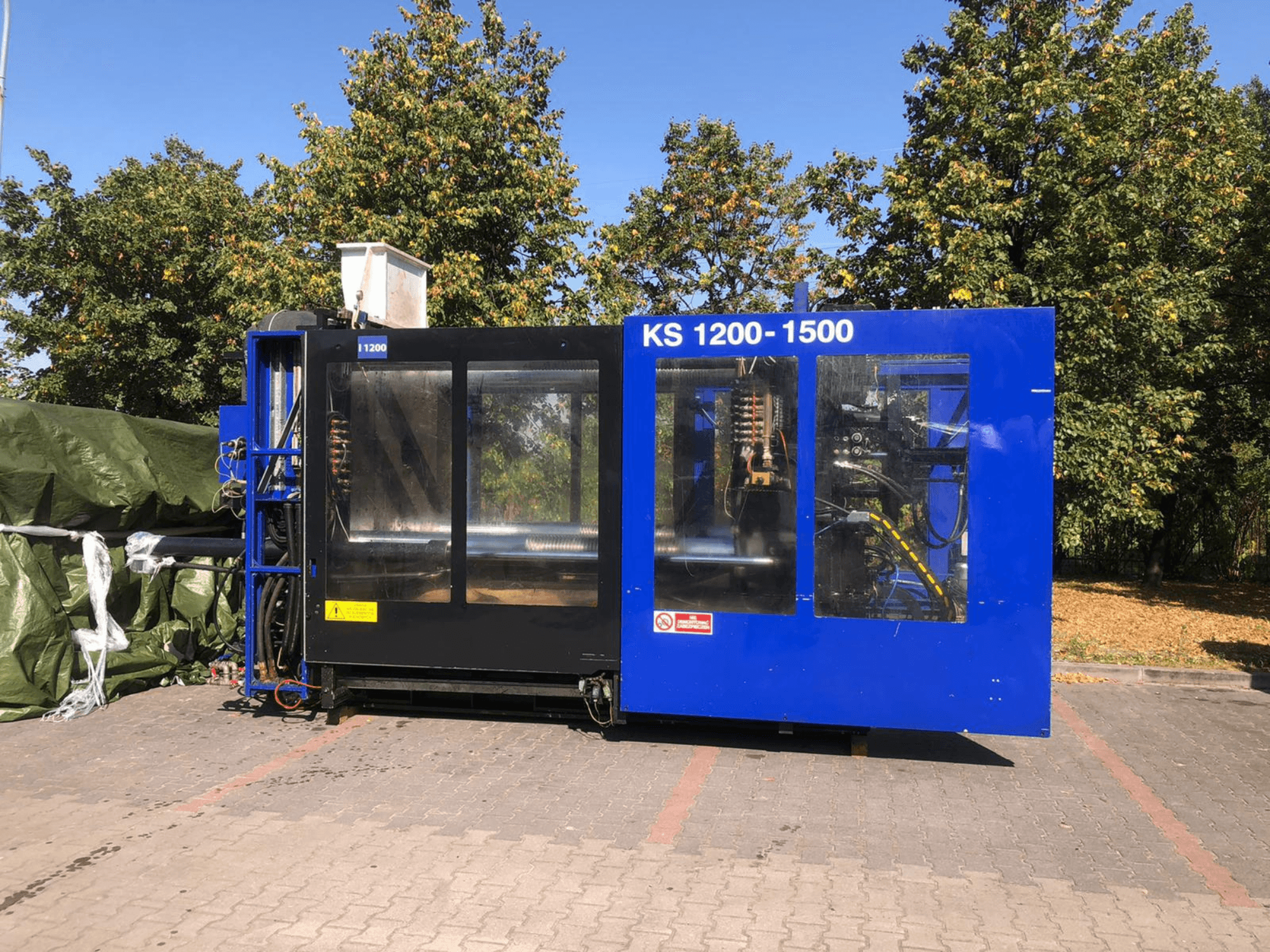 Hydraulinen ruiskupuristuskone ITALTECH KS 1200 8300 ES, sivukuva, jossa näkyy hallintalaitteet ja koneen yksityiskohdat puistomaisessa ympäristössä.